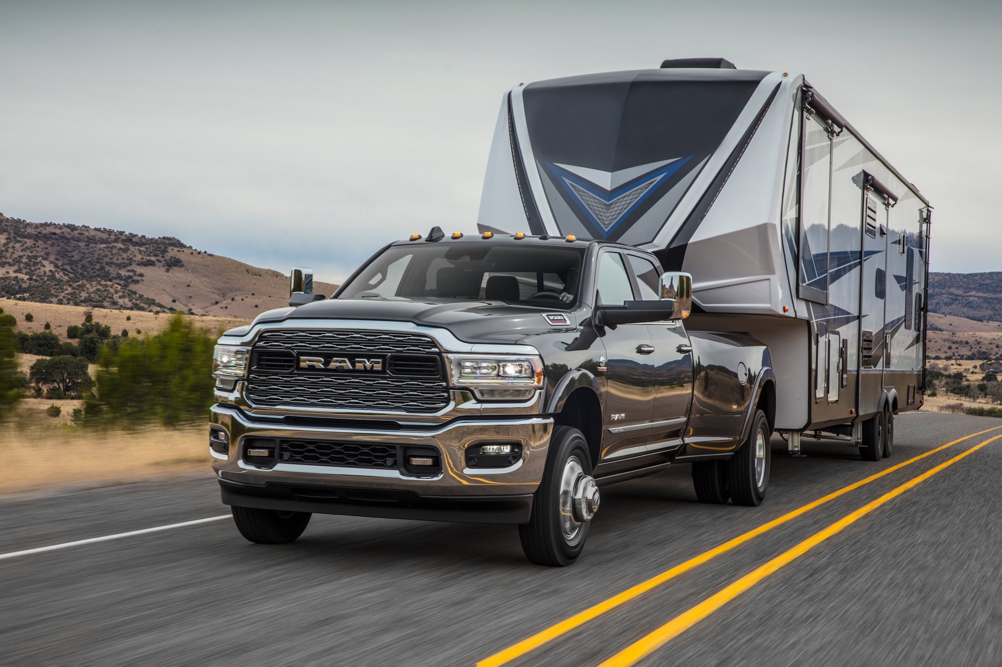 2023 Ram 3500 is towing a travel trailer down a rural highway.