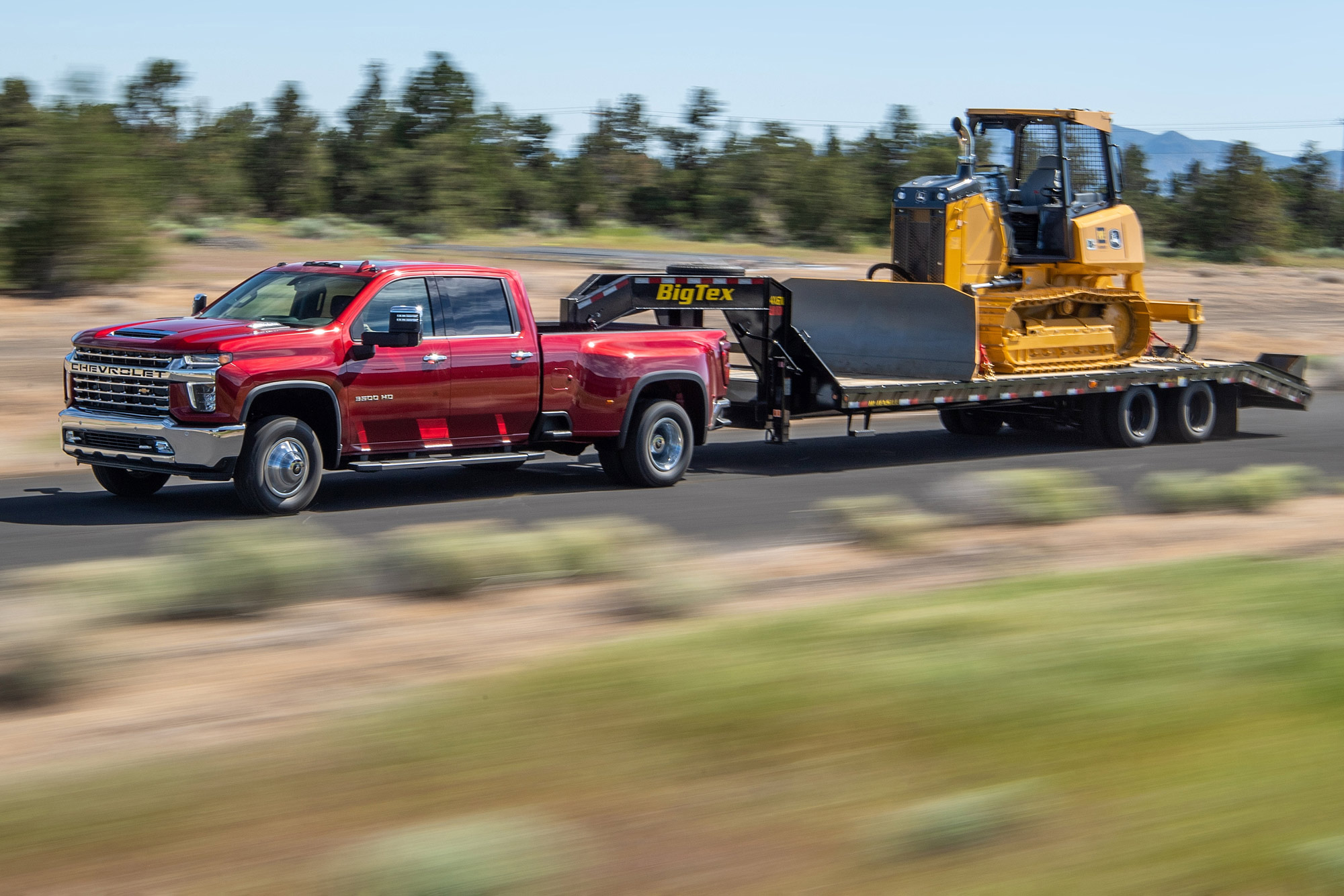 Red 2023 Chevrolet Silverado 3500 tows a bulldozer on a trailer.