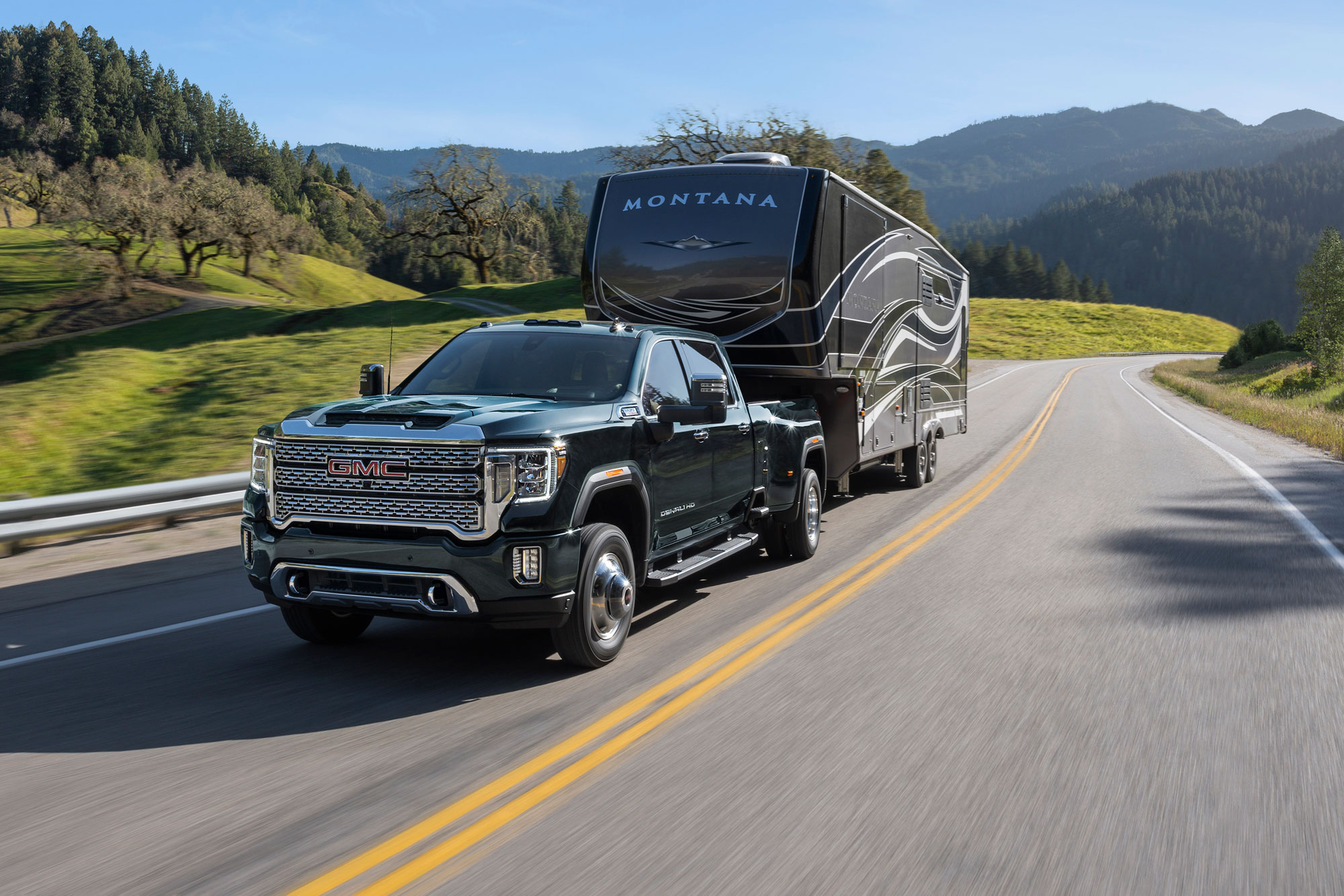 2023 GMC Sierra 3500 tows a travel trailer down a scenic rural highway.