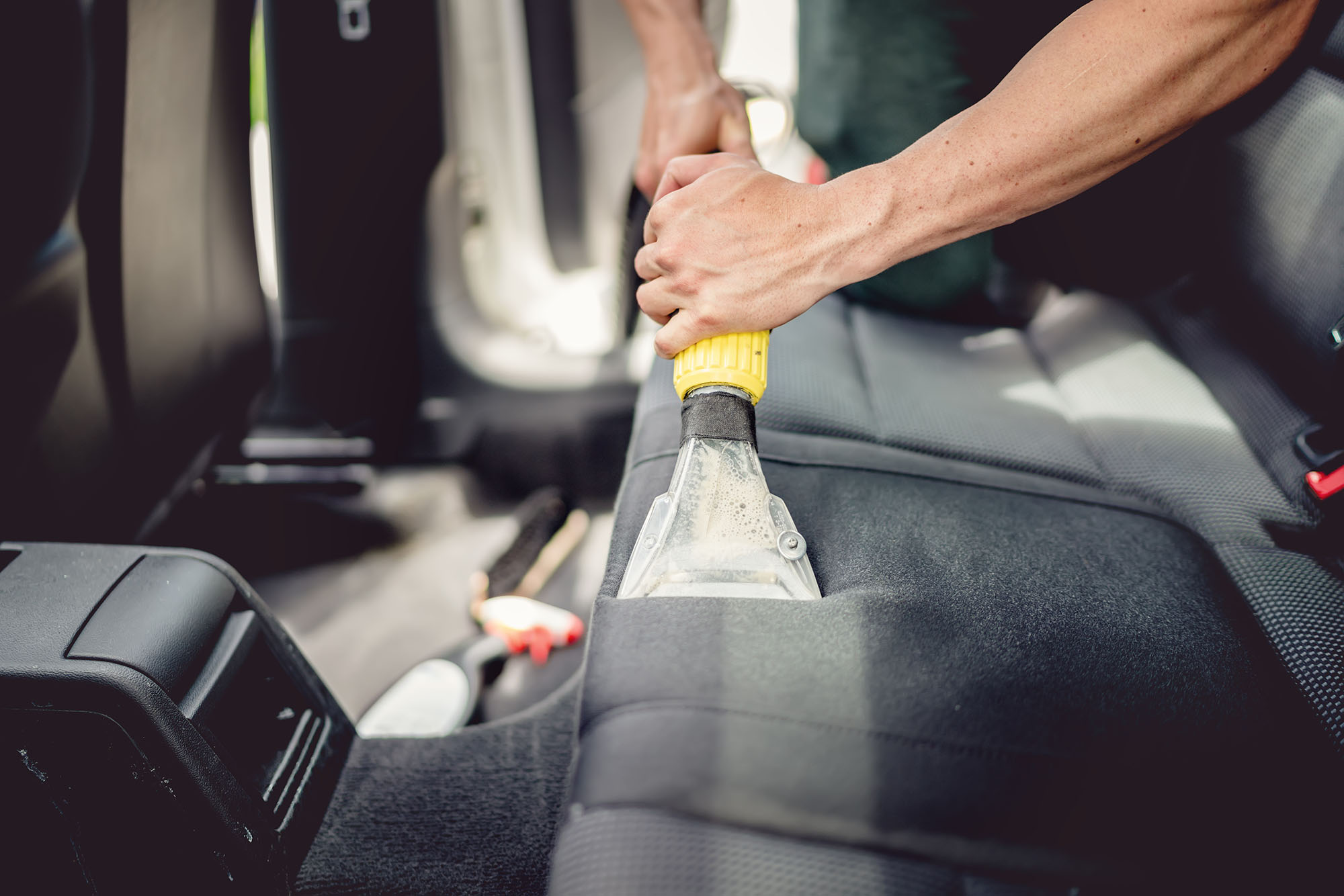 A person uses an upholstery cleaning machine to clean the back seat of a car.