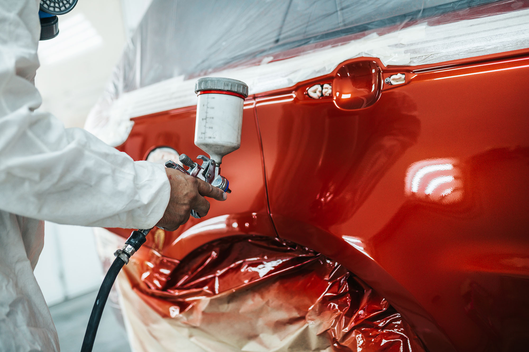 A person sprays orange-red paint onto a vehicle door panel