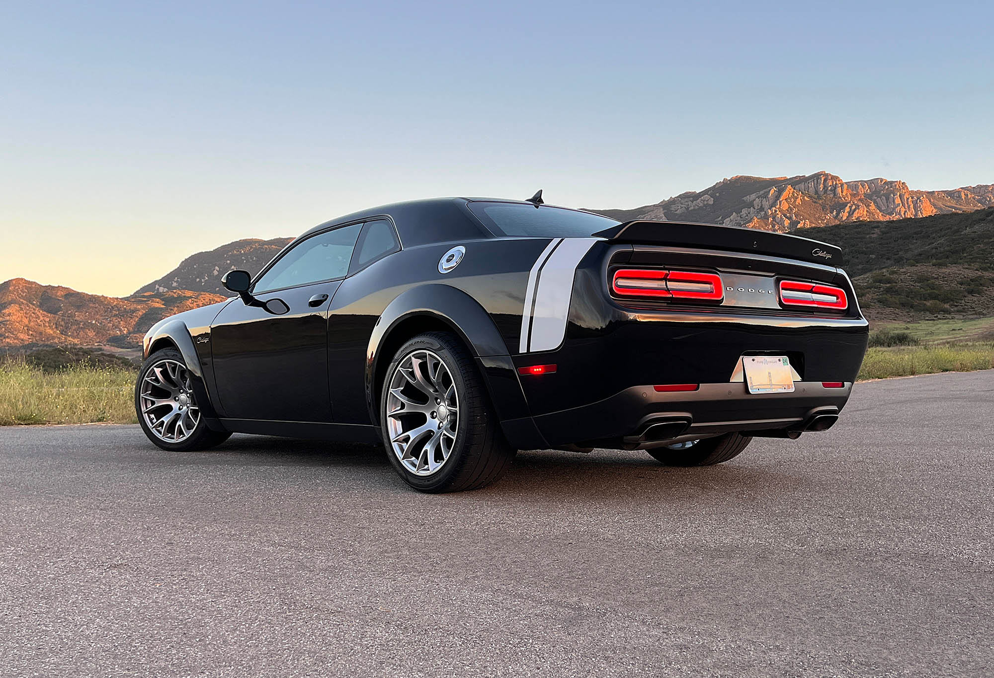 2023 Dodge Challenger Black Ghost rear three-quarter view with mountains in the background.