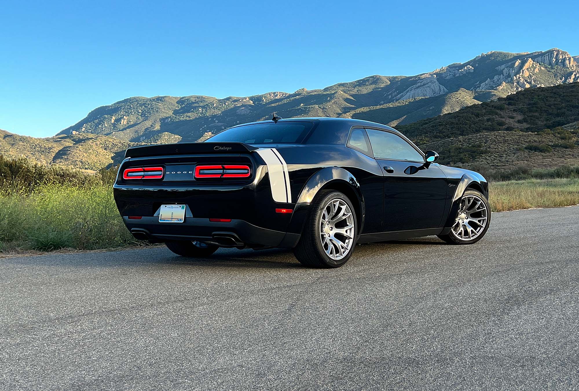 2023 Dodge Challenger Black Ghost rear three-quarter view with mountains in the background.