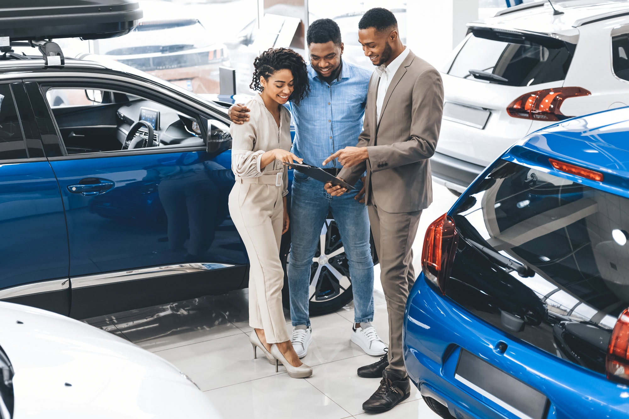 Black couple visiting dealership and talking with salesman in auto showroom