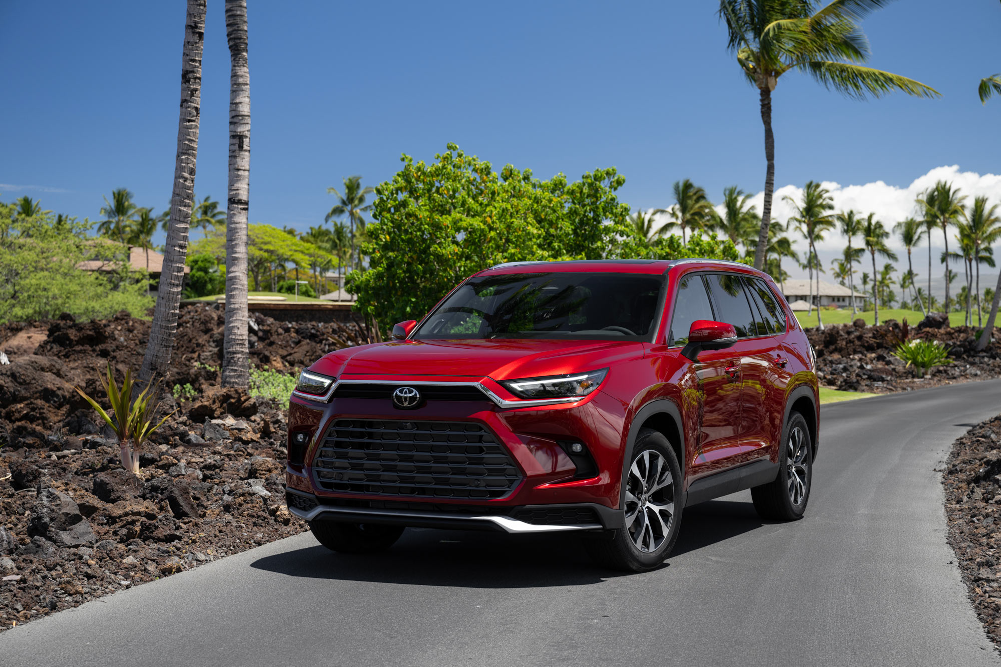 Red 2024 Toyota Grand Highlander parked by palm trees on road.