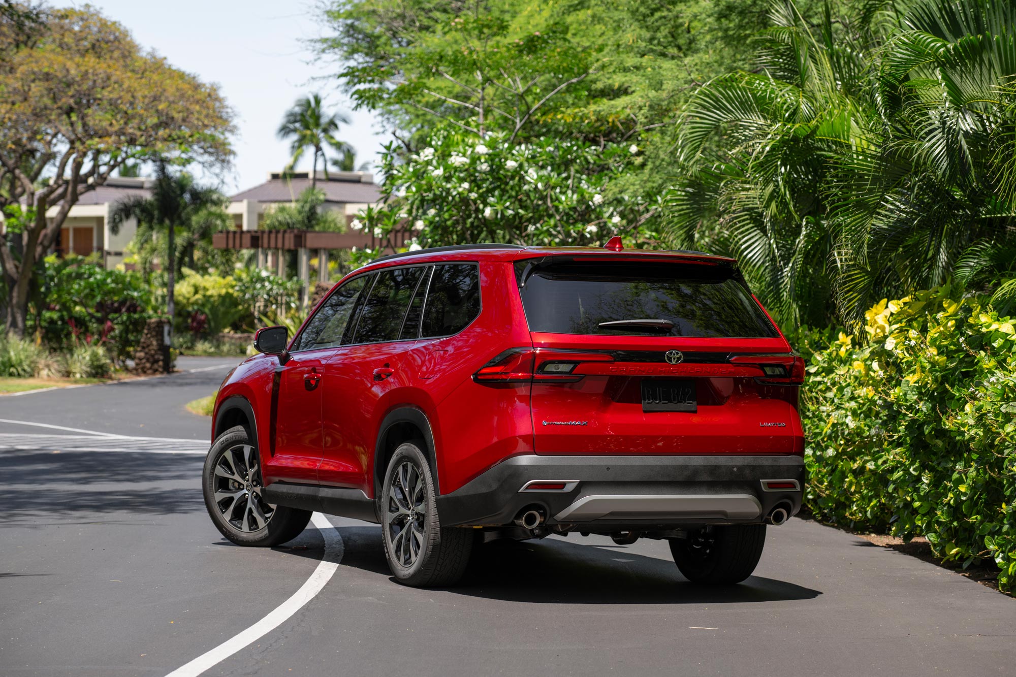 2024 Toyota Grand Highlander in red parked near plants and bushes.