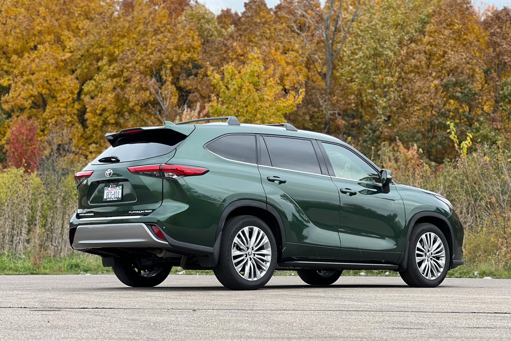 2024 Toyota Highlander in green parked on concrete by dense trees.