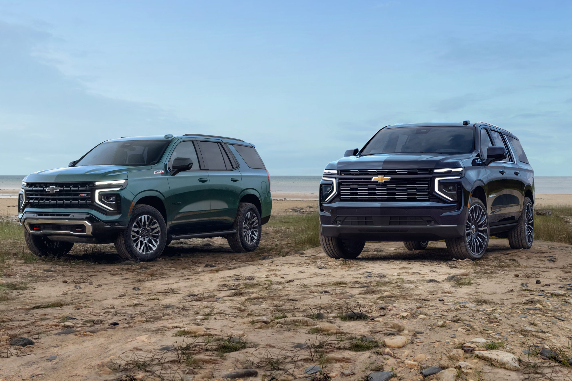 2025 Chevrolet Tahoe and Chevrolet Suburban parked on sand by a beach.