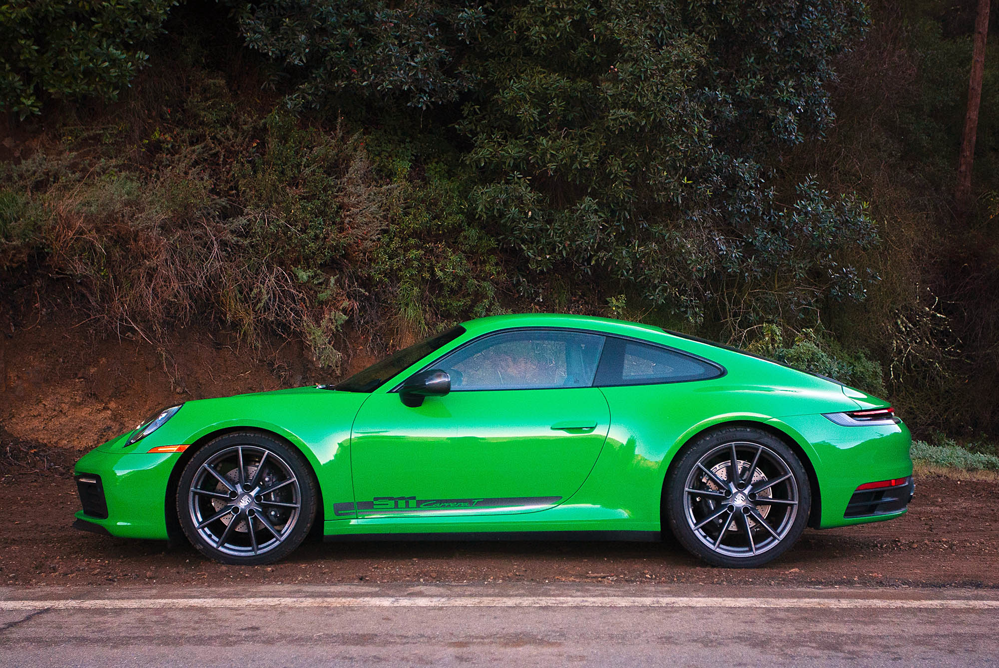  2023 Porsche 911 Carrera T in Python Green parked beside a road, side view.