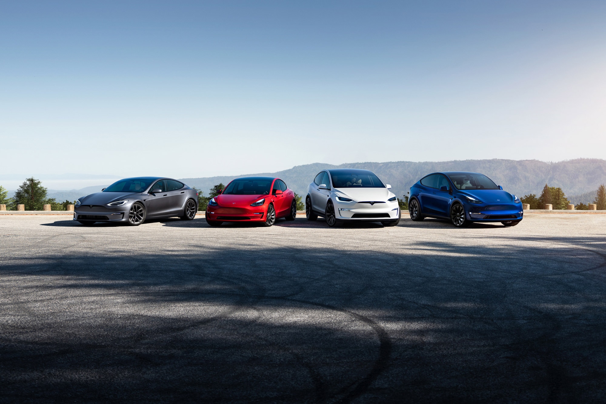 Four Tesla vehicles are parked side by side in a parking lot.