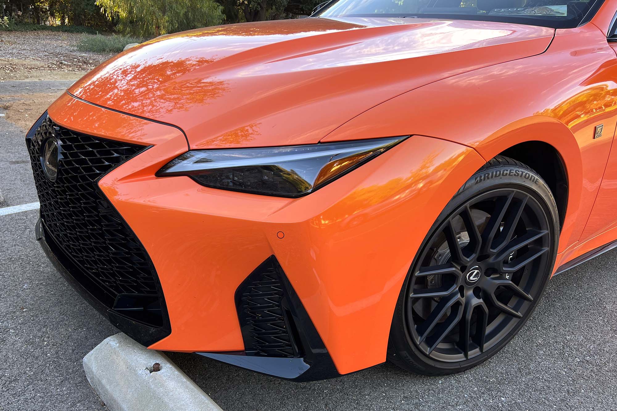 Detail view of an orange 2023 Lexus IS 500 front end over a parking curb