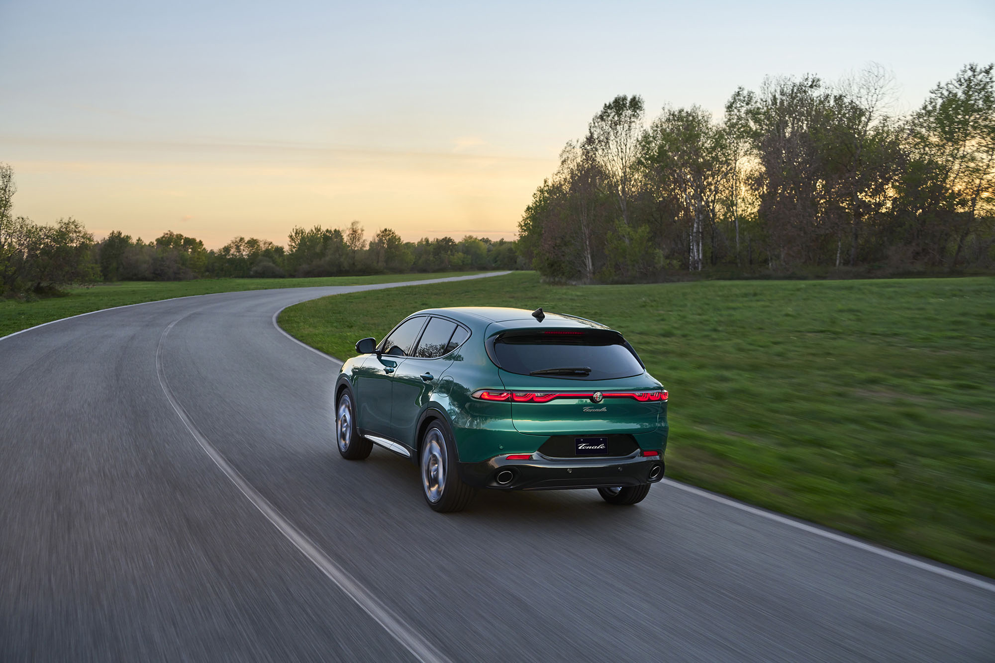Green Alfa Romeo Tonale driving down paved road next to grass