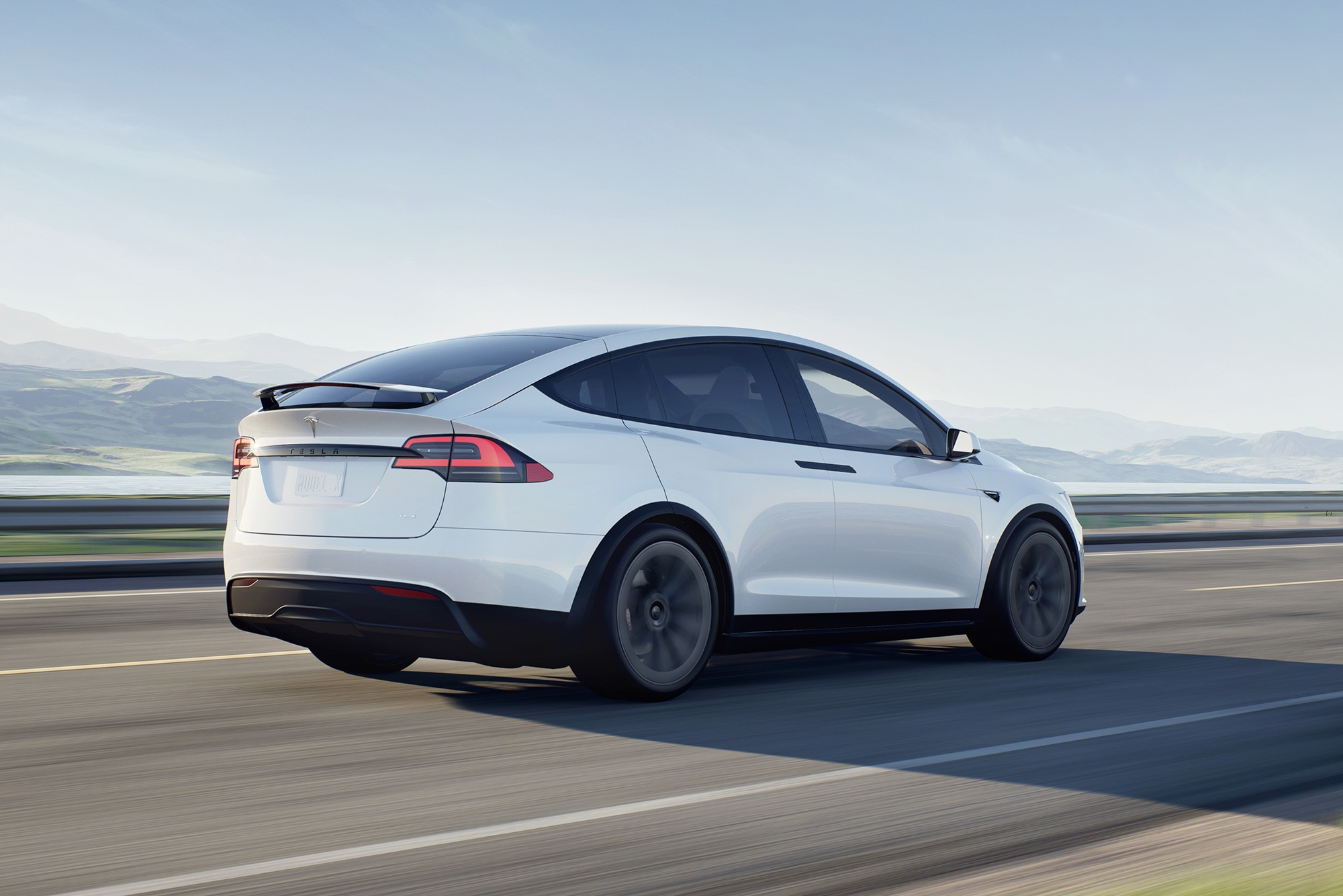 Tesla Model X in white driving near mountains.