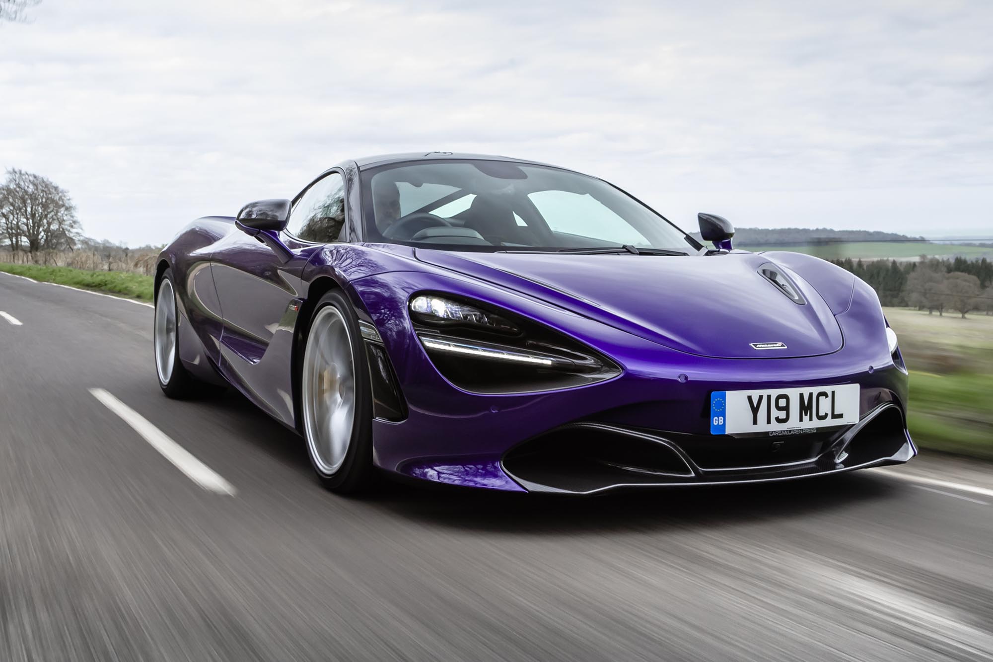 Front right quarter view of a purple McLaren 720S driving on country road.