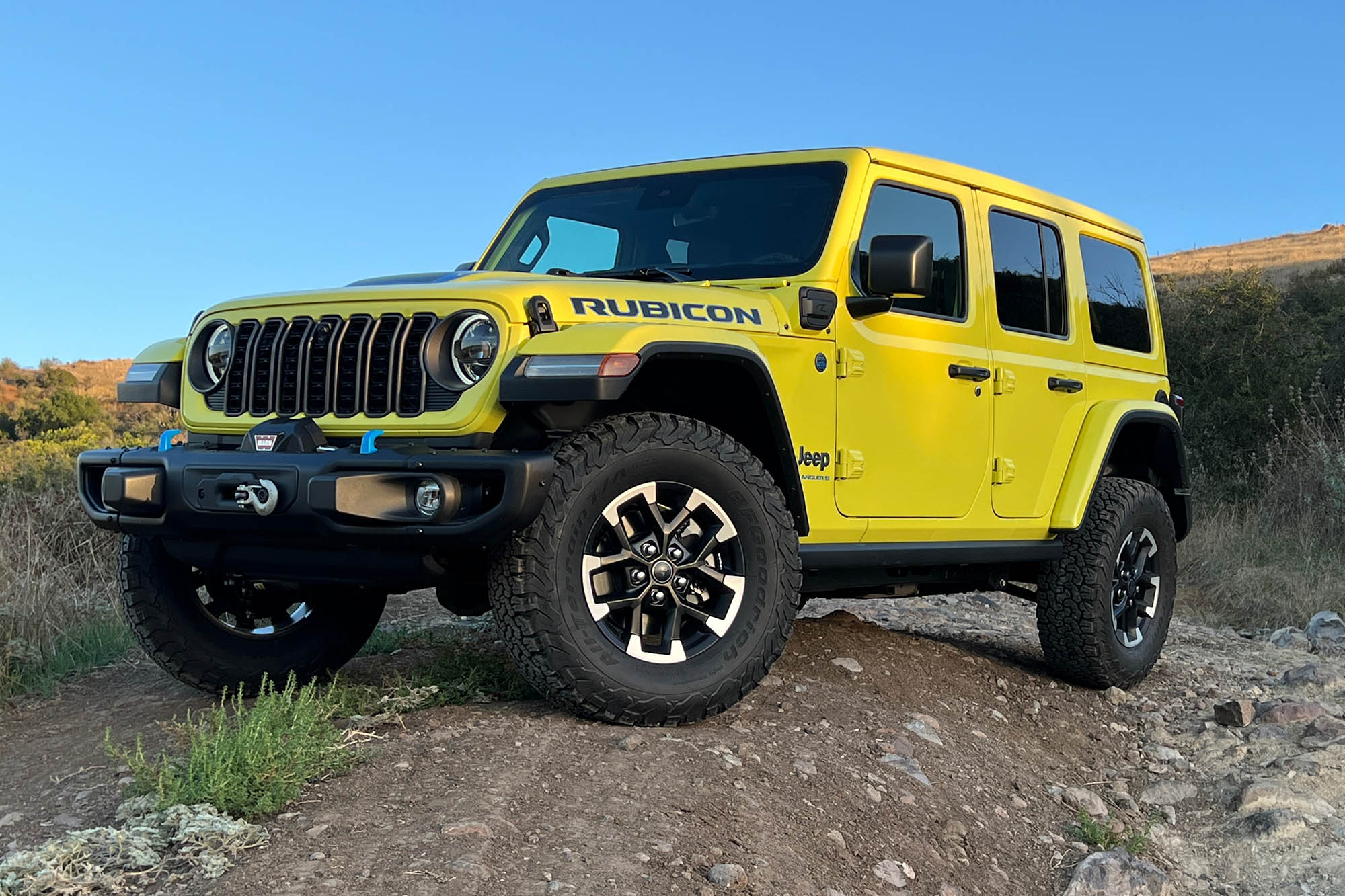 Front left quarter view of a yellow 2024 Jeep Wrangler Rubicon 4xe on a rocky trail