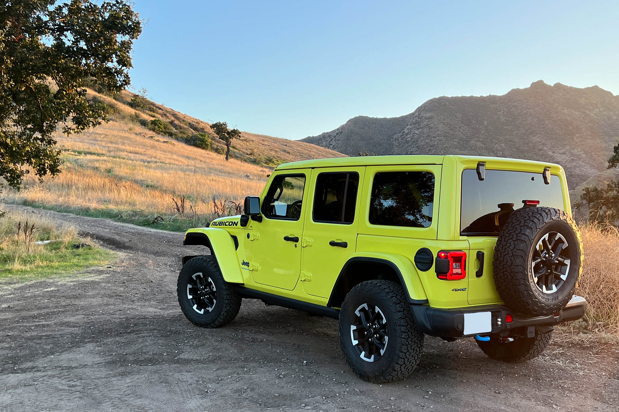 Rear left quarter view of a yellow 2024 Jeep Wrangler Rubicon 4xe parked on a mountain trail