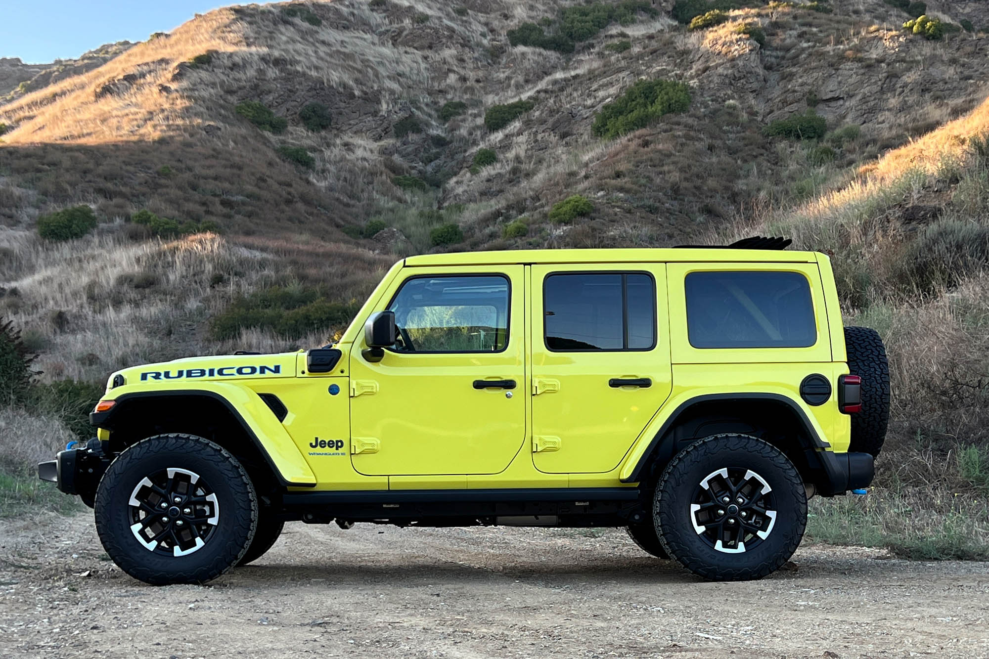 Side view of a yellow 2024 Jeep Wrangler Rubicon 4xe on a mountain trail