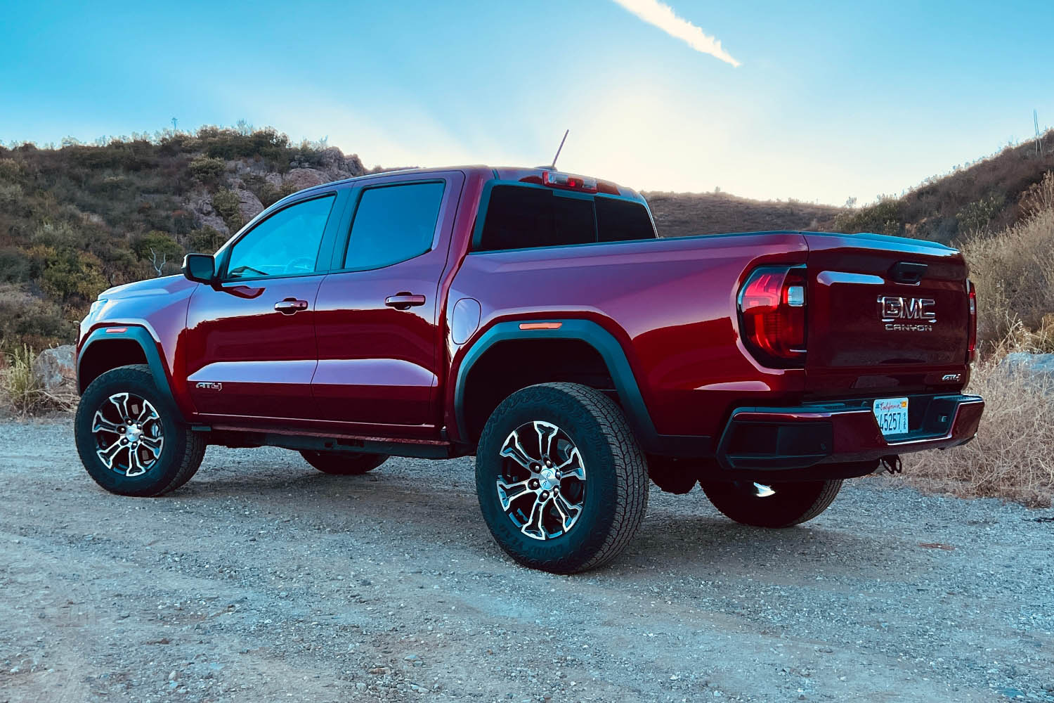 Rear left view of a red 2023 GMC Canyon parked on dirt road.