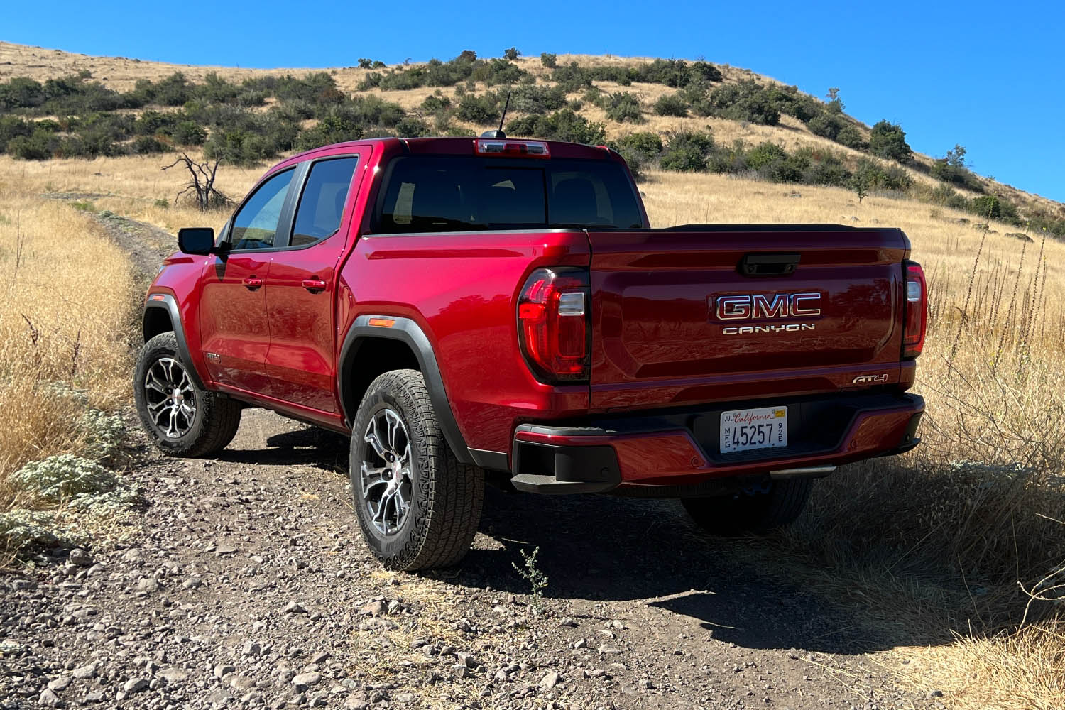 Rear left quarter view of a red 2023 GMC Canyon on an off-road trail 