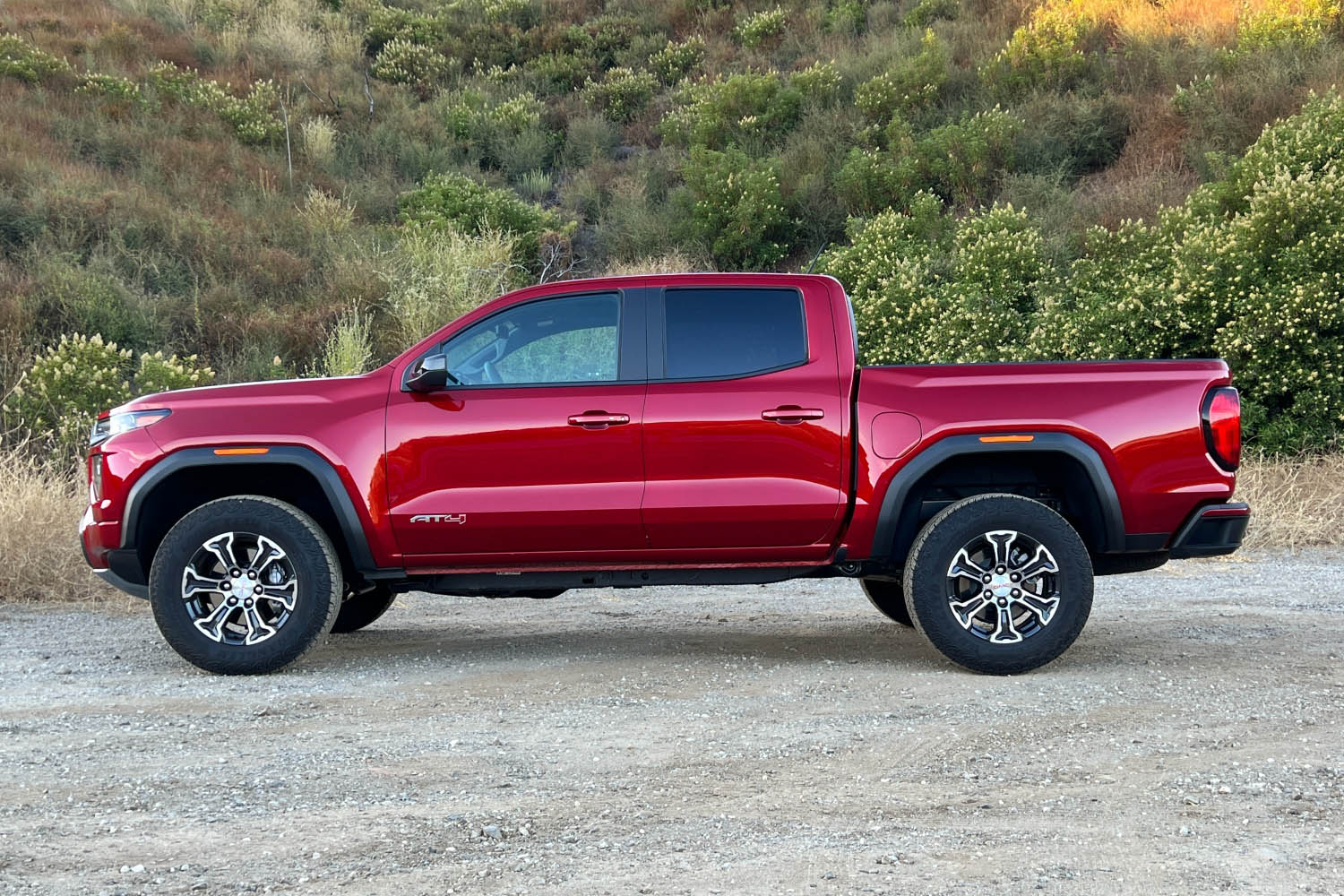 Side view of a red 2023 GMC Canyon parked on a dirt road 