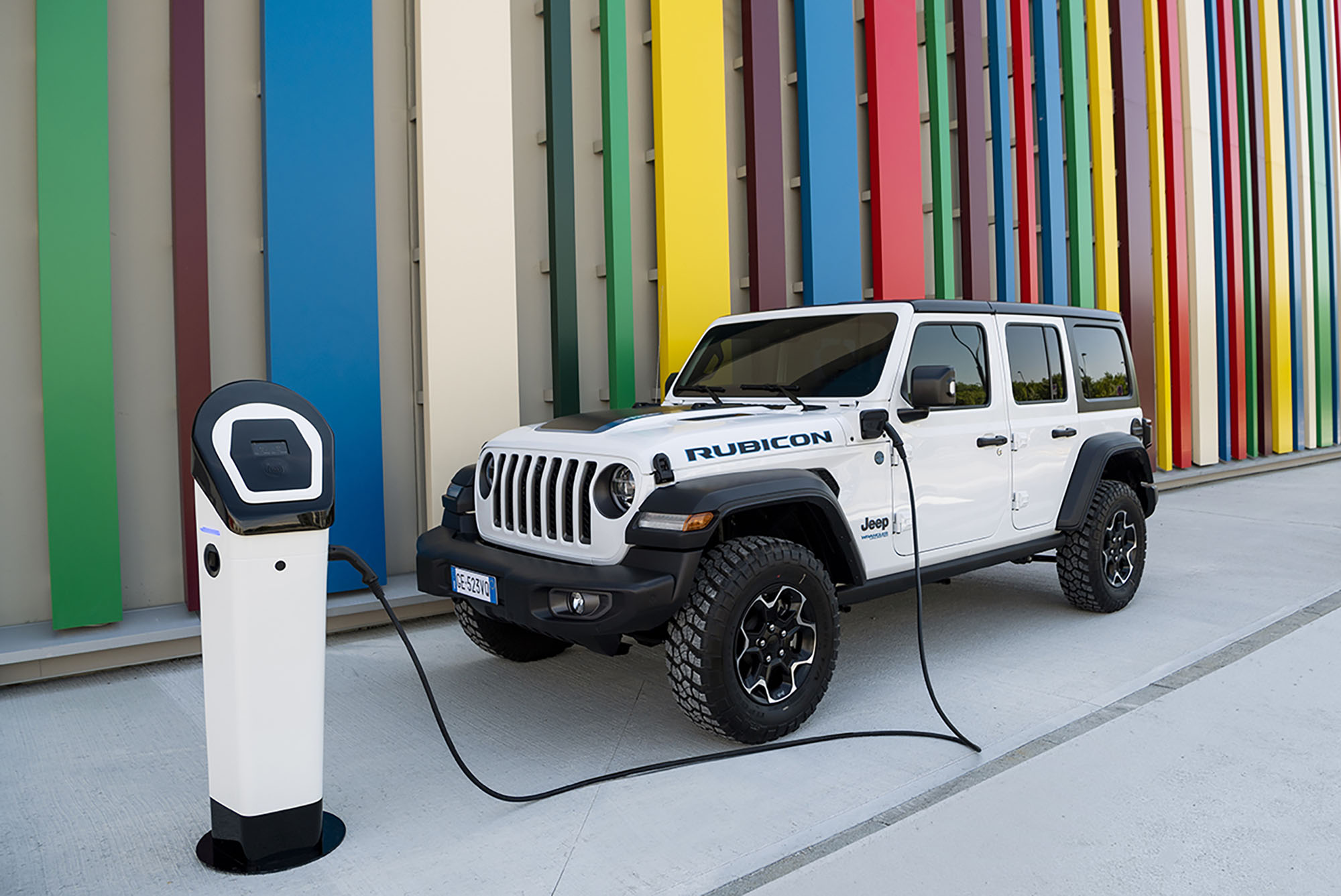 A white Jeep Wrangler 4xe plugged into charger in front of a multicolored wall