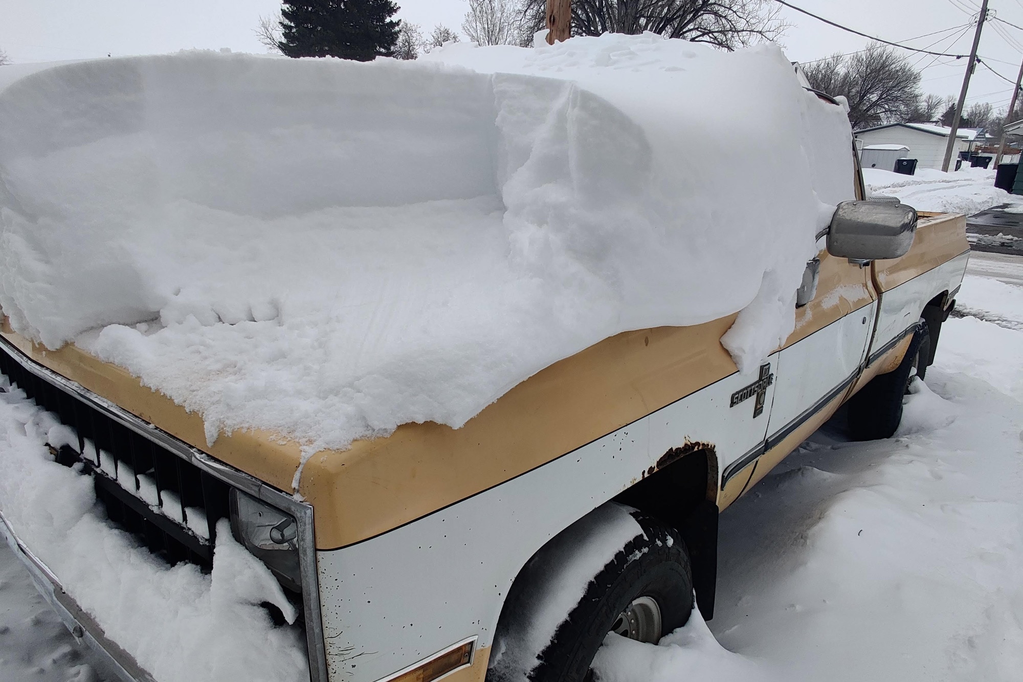 An older yellow and white Chevrolet pickup truck covered in snow