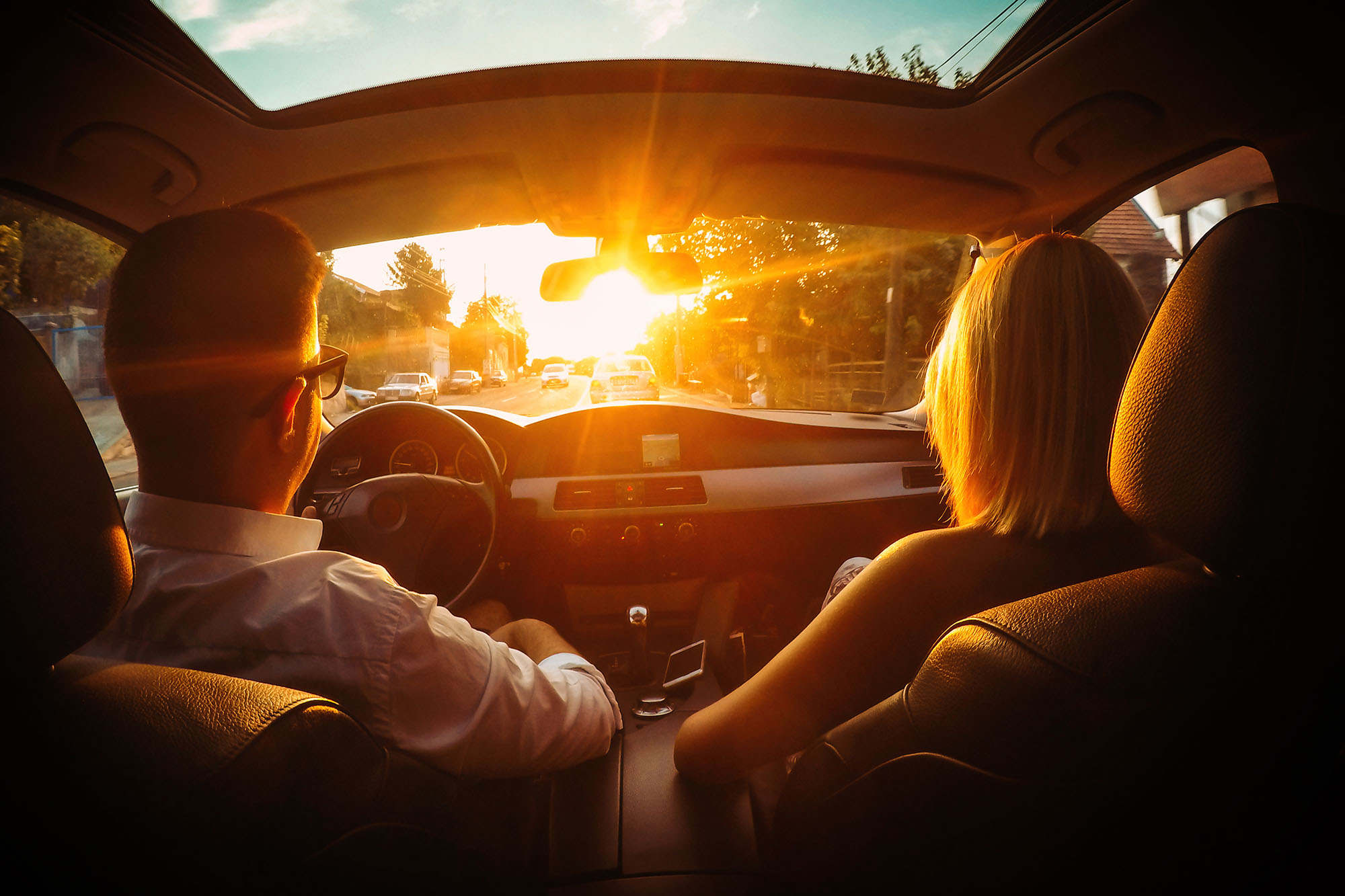 Two people in a car driving into the sun