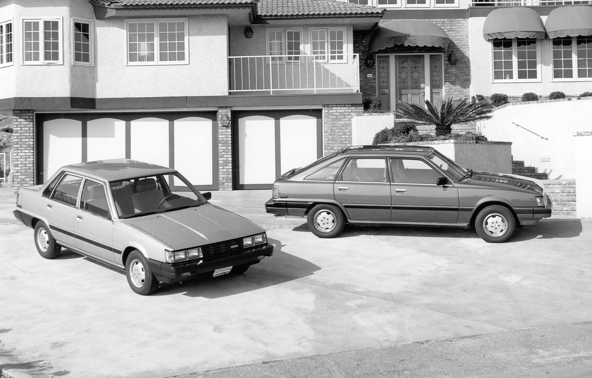 A 1980s Toyota Camry sedan and hatchback parked in front of a house.