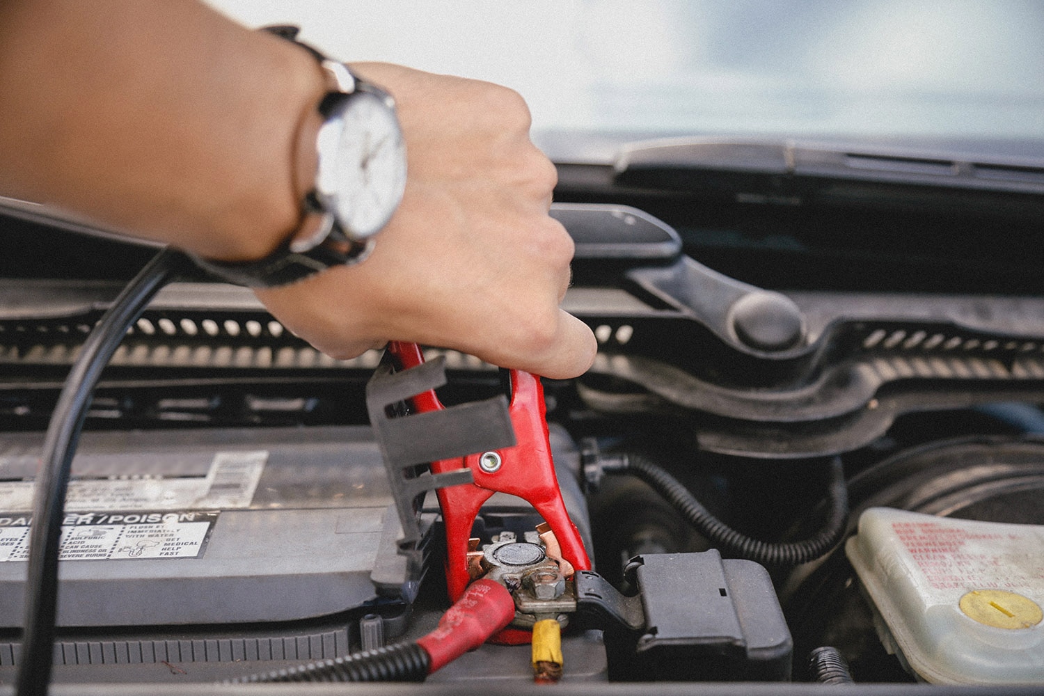 A person's hand attaches a jumper cable to a battery terminal