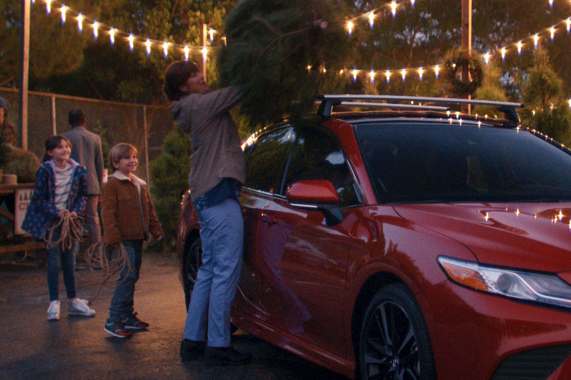 A person placing a Christmas tree on a red Toyota Camry in a television advertisement