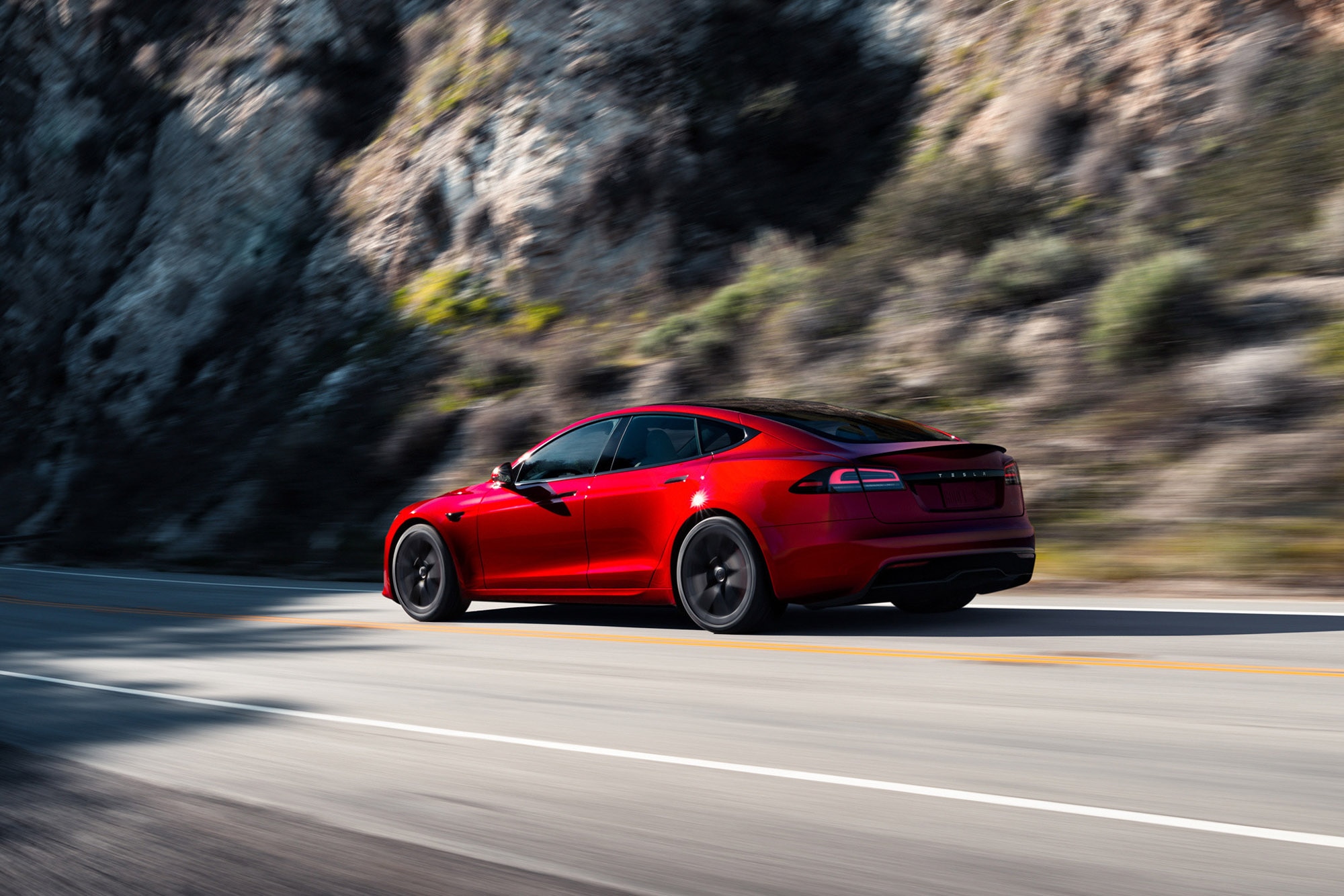 Red Tesla Model S driving on a two-lane mountain highway
