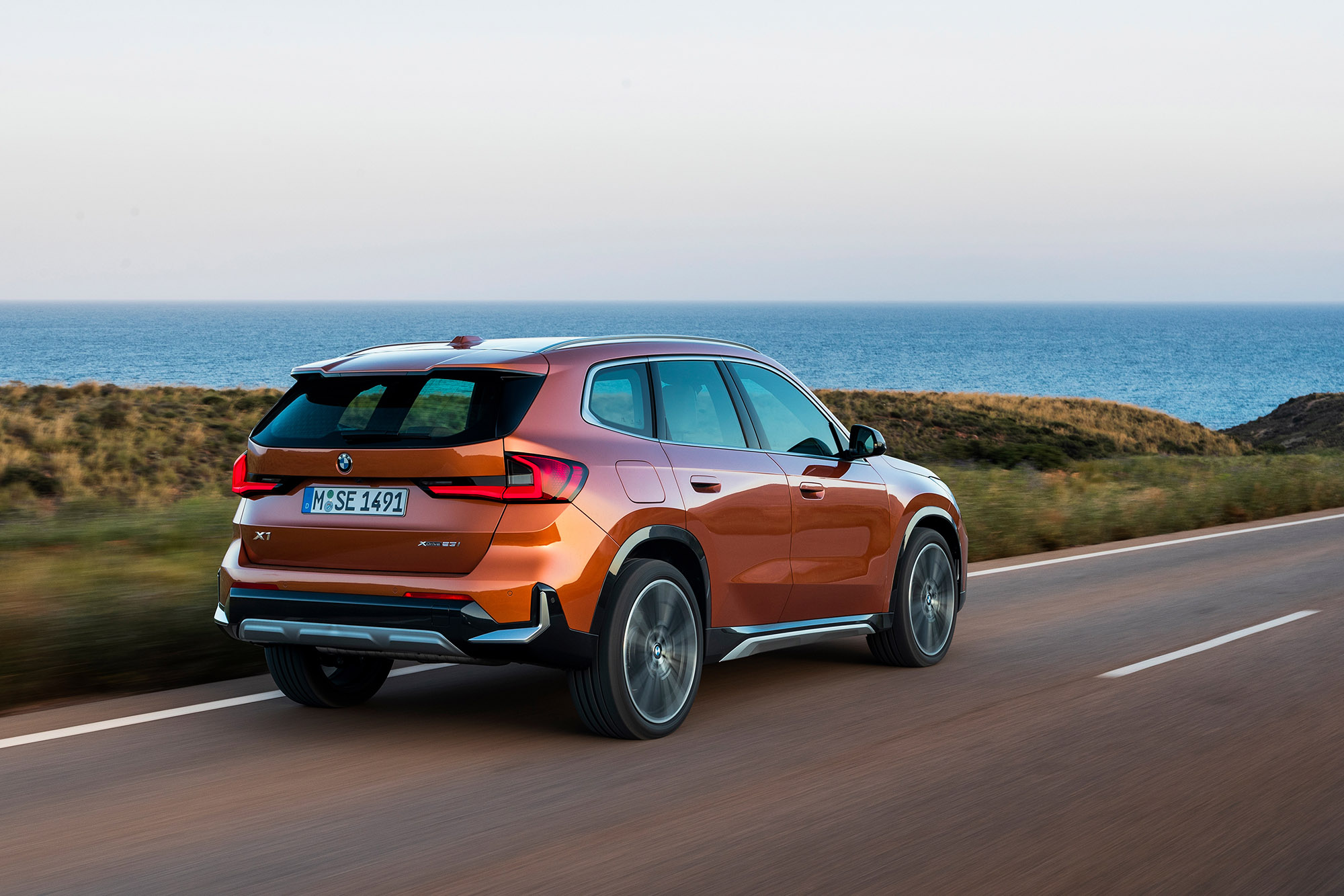 2023 BMW X1 in orange driving along a coastal road