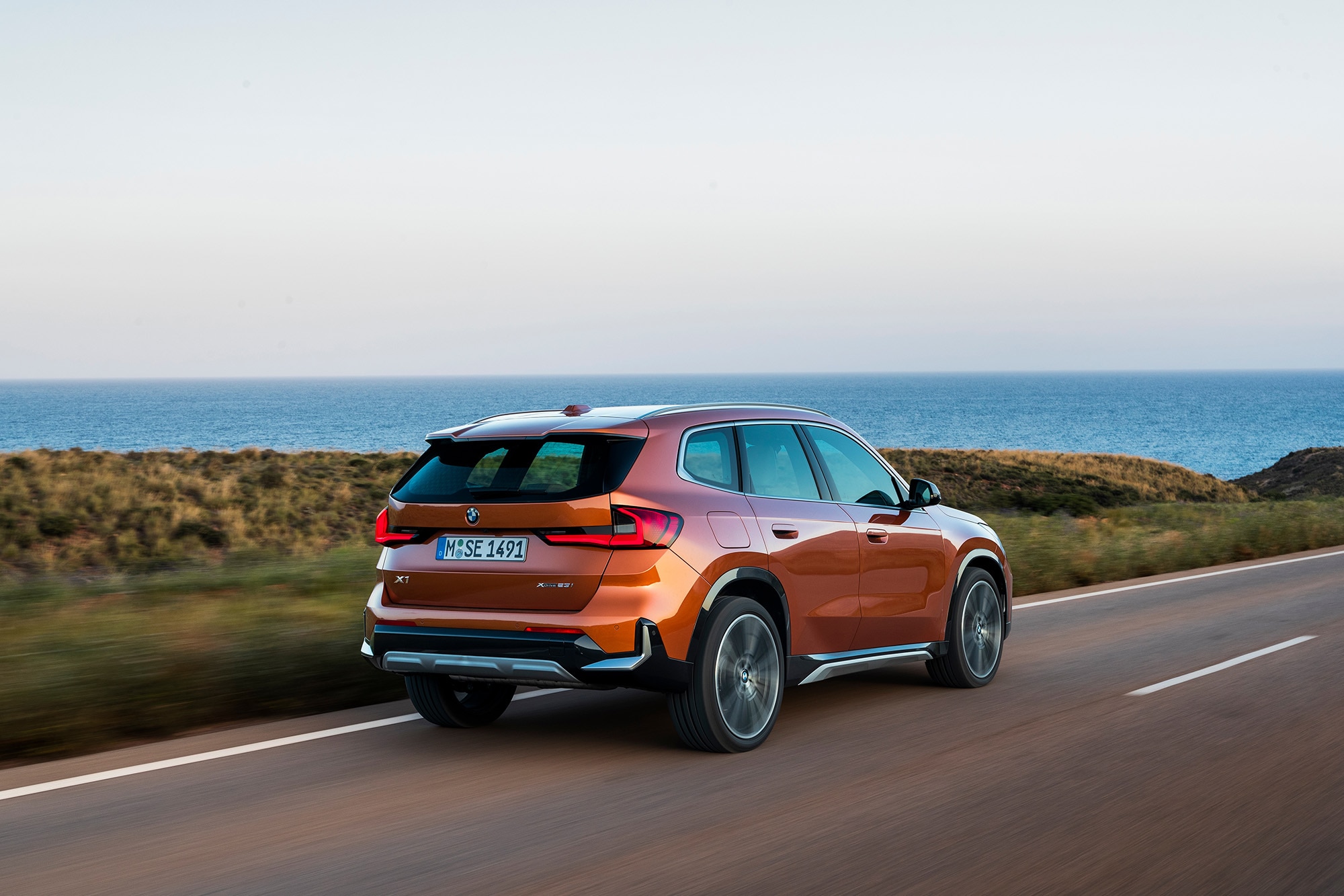 2023 BMW X1 in orange driving along a coastal road