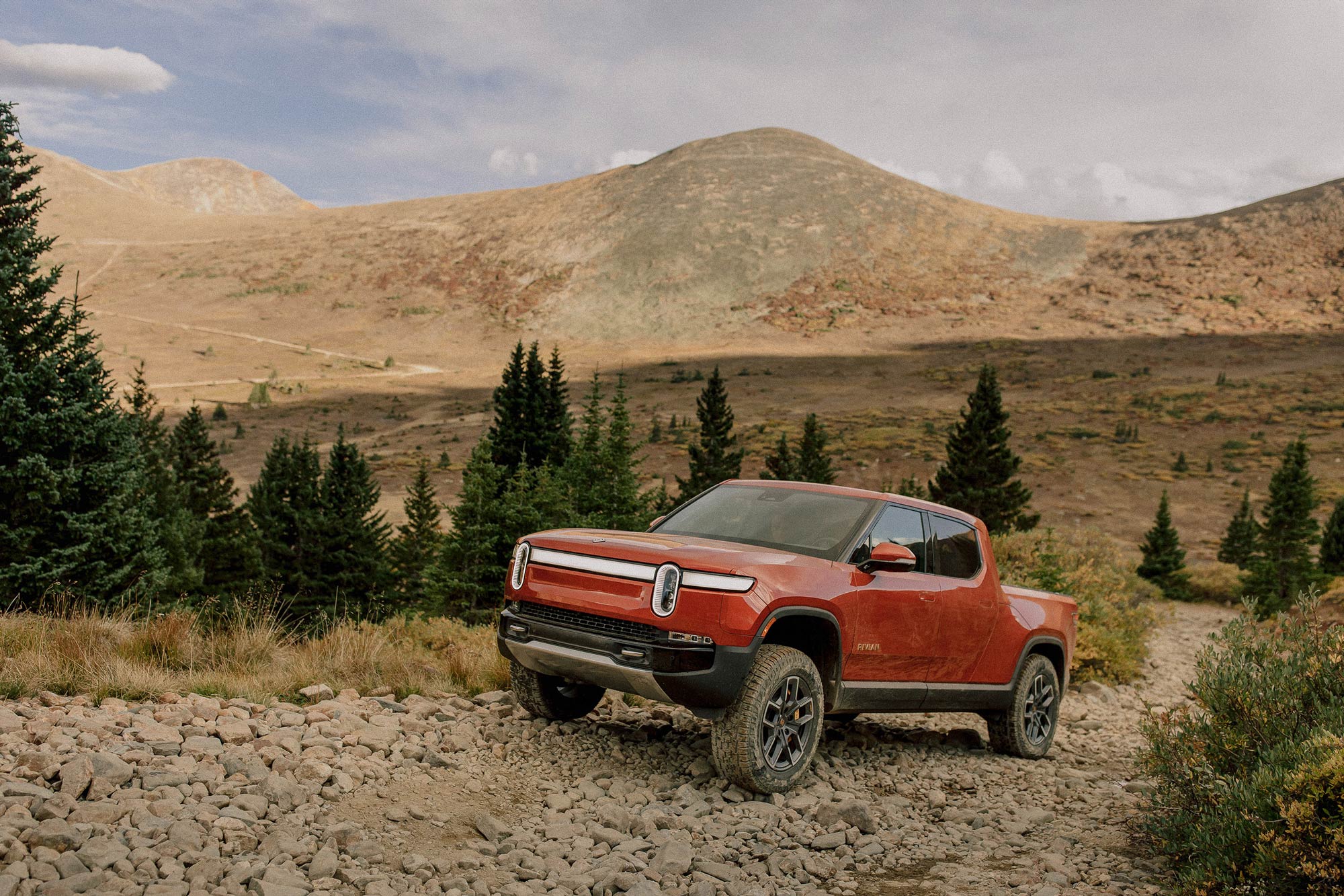 Rivian R1T electric pickup truck drives up a rocky trail off-road.