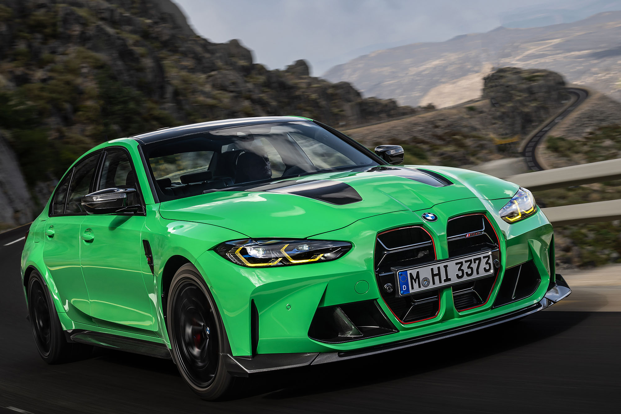 A green 2024 BMW M3 driving on a mountain road