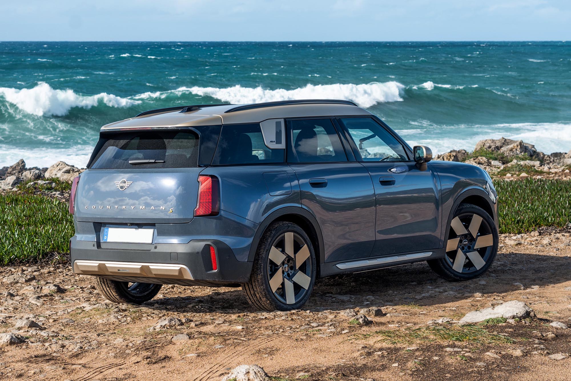 Right rear quarter view of a blue 2025 Mini Countryman SE with a white roof in front of the ocean