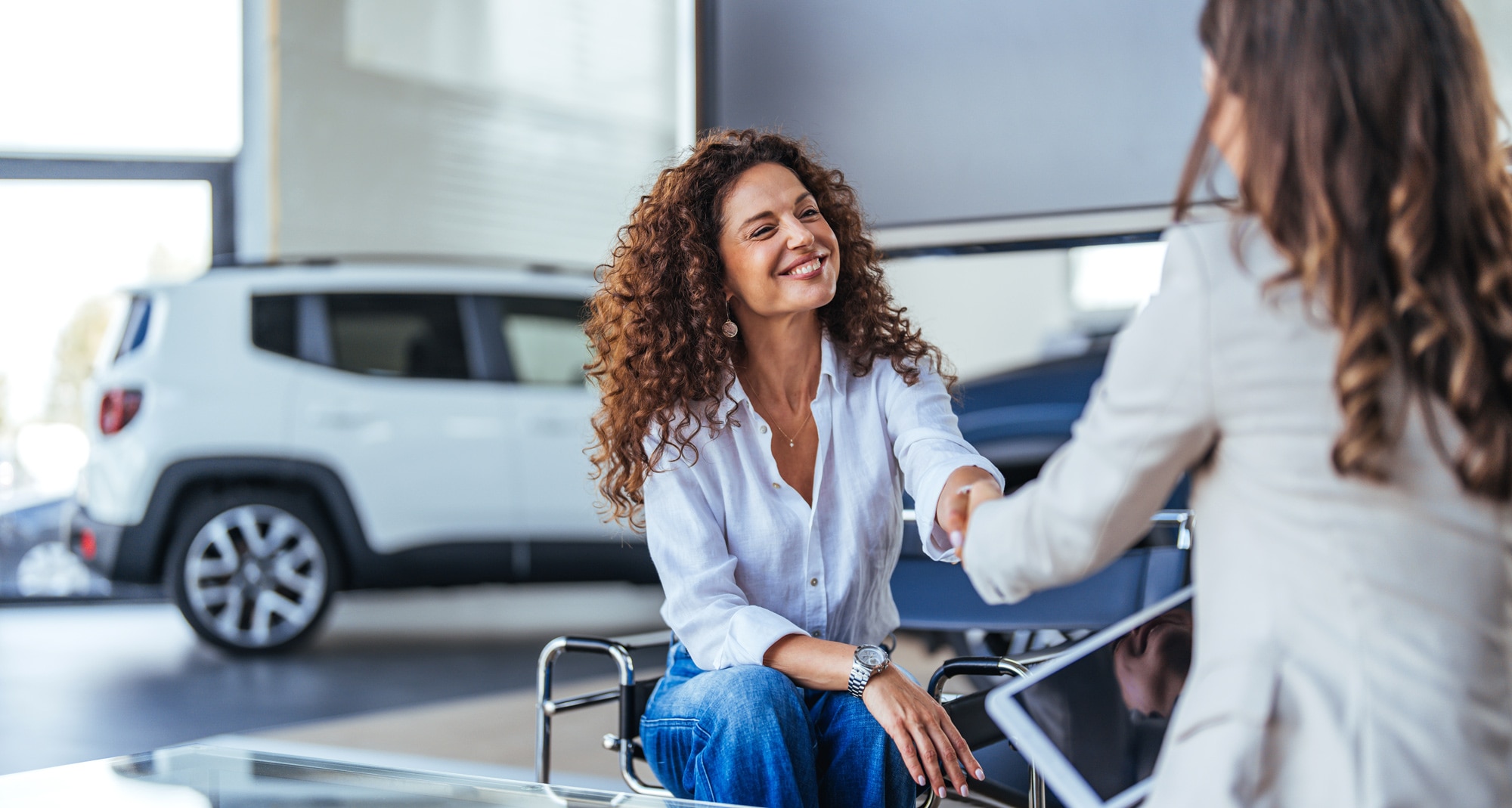 Smiling women shaking hands at a car dealership
