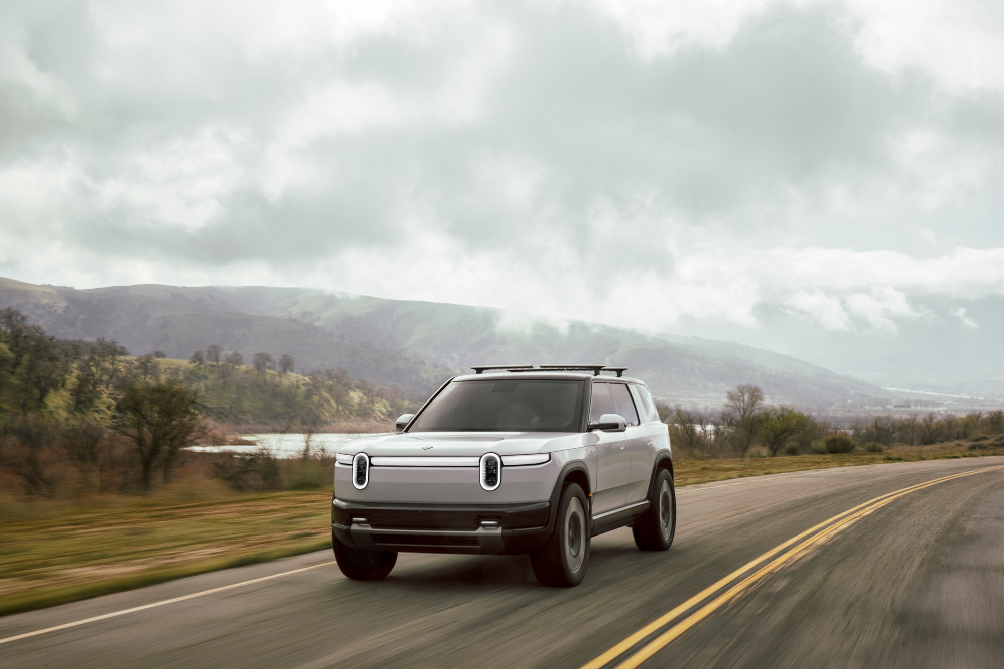 White 2026 Rivian R2 driving on country road.