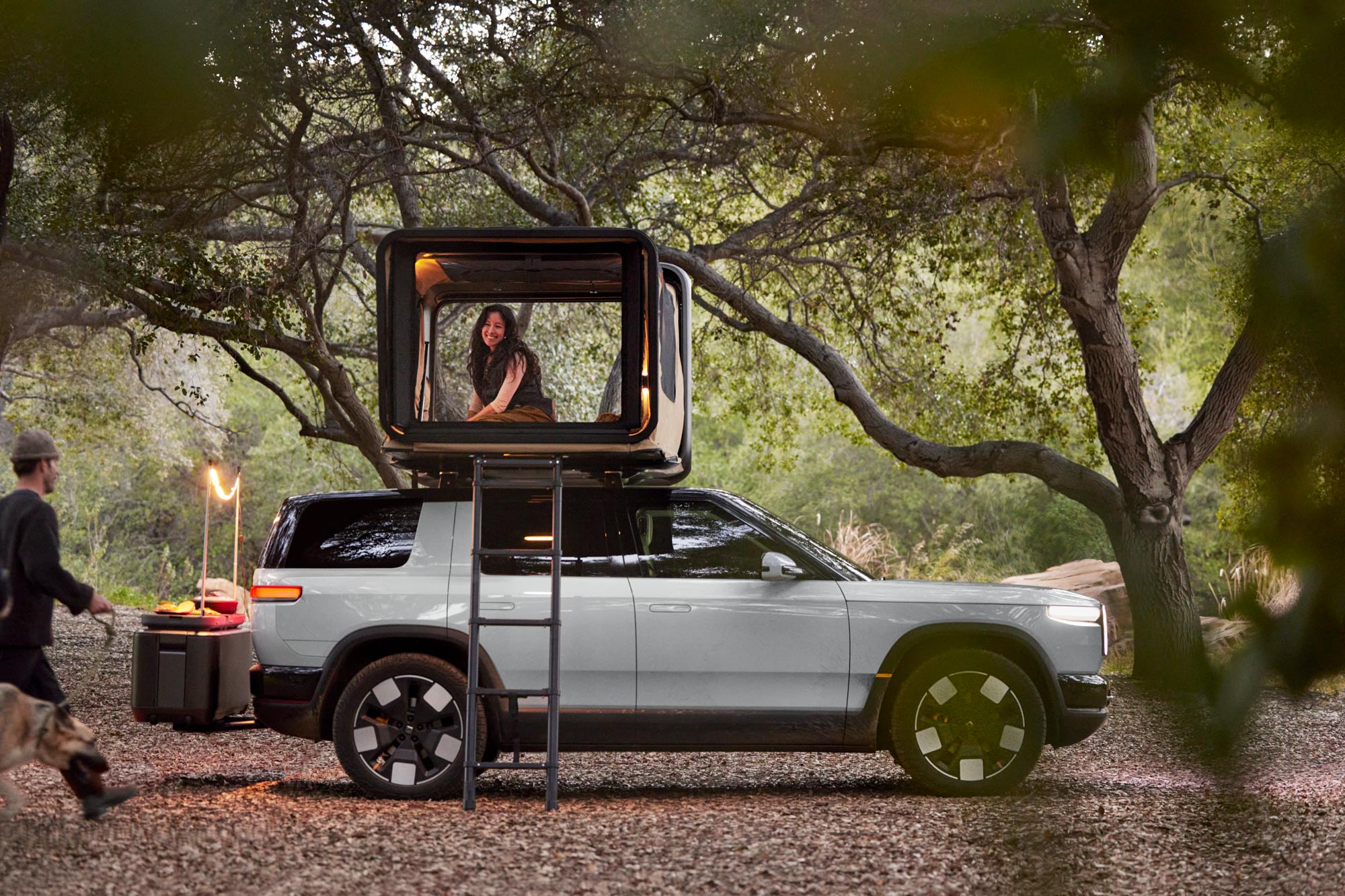 2026 Rivian R2 with rooftop tent set up and a person inside.