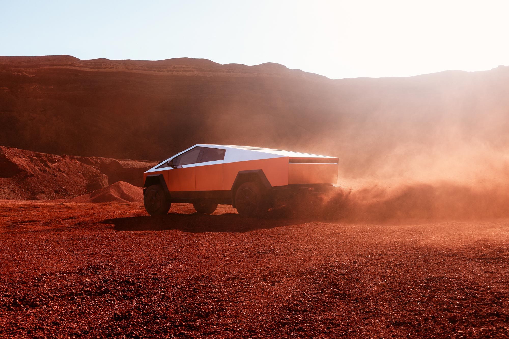 2024 Tesla Cybertruck driving in red dirt throwing up dust.