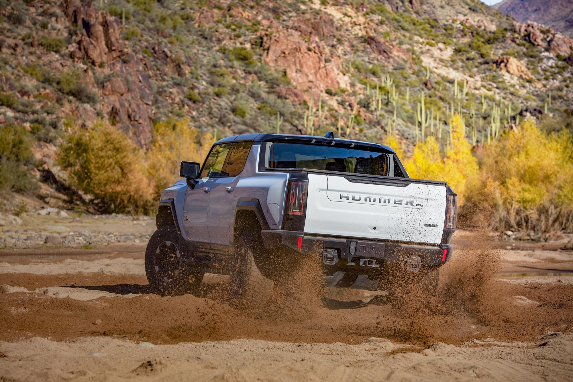 2024 GMC Hummer EV Pickup throws up dirt and sand off road.