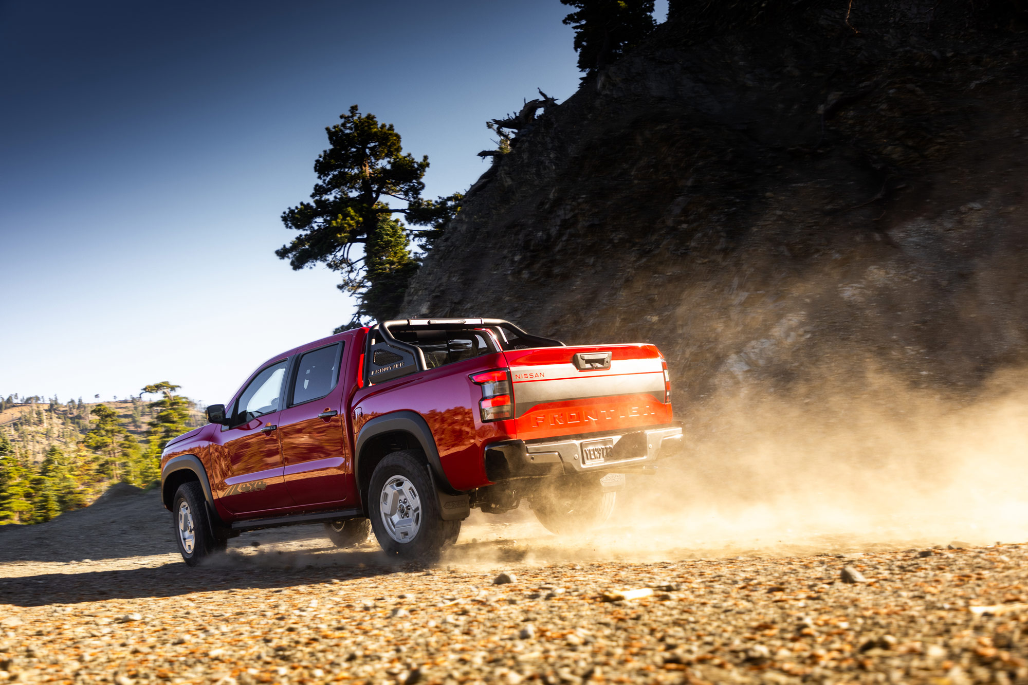 Red 2024 Nissan Frontier driving down dirt path.