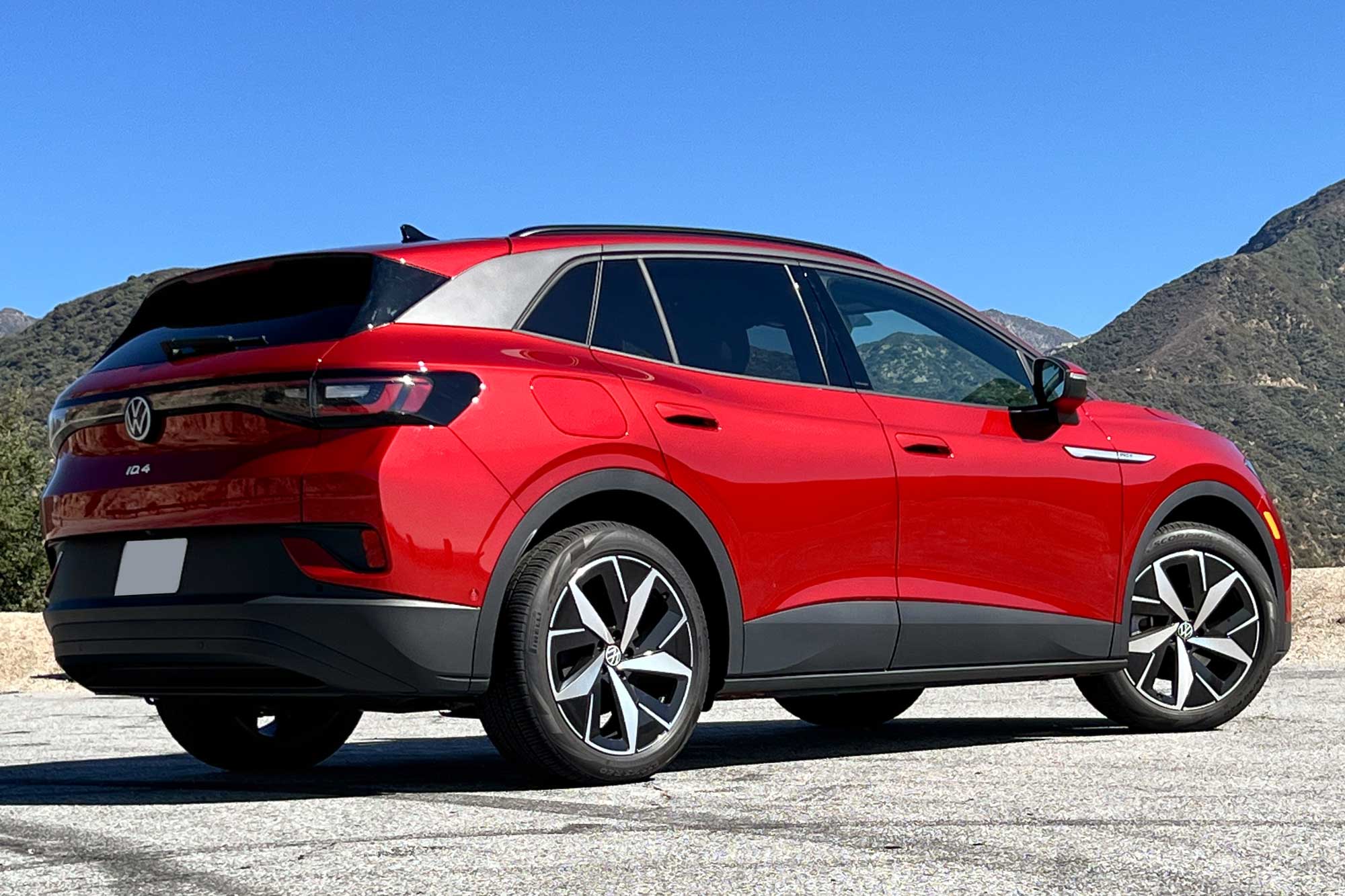 Rear quarter view of a red 2024 Volkswagen ID.4 parked on pavement near some mountains.