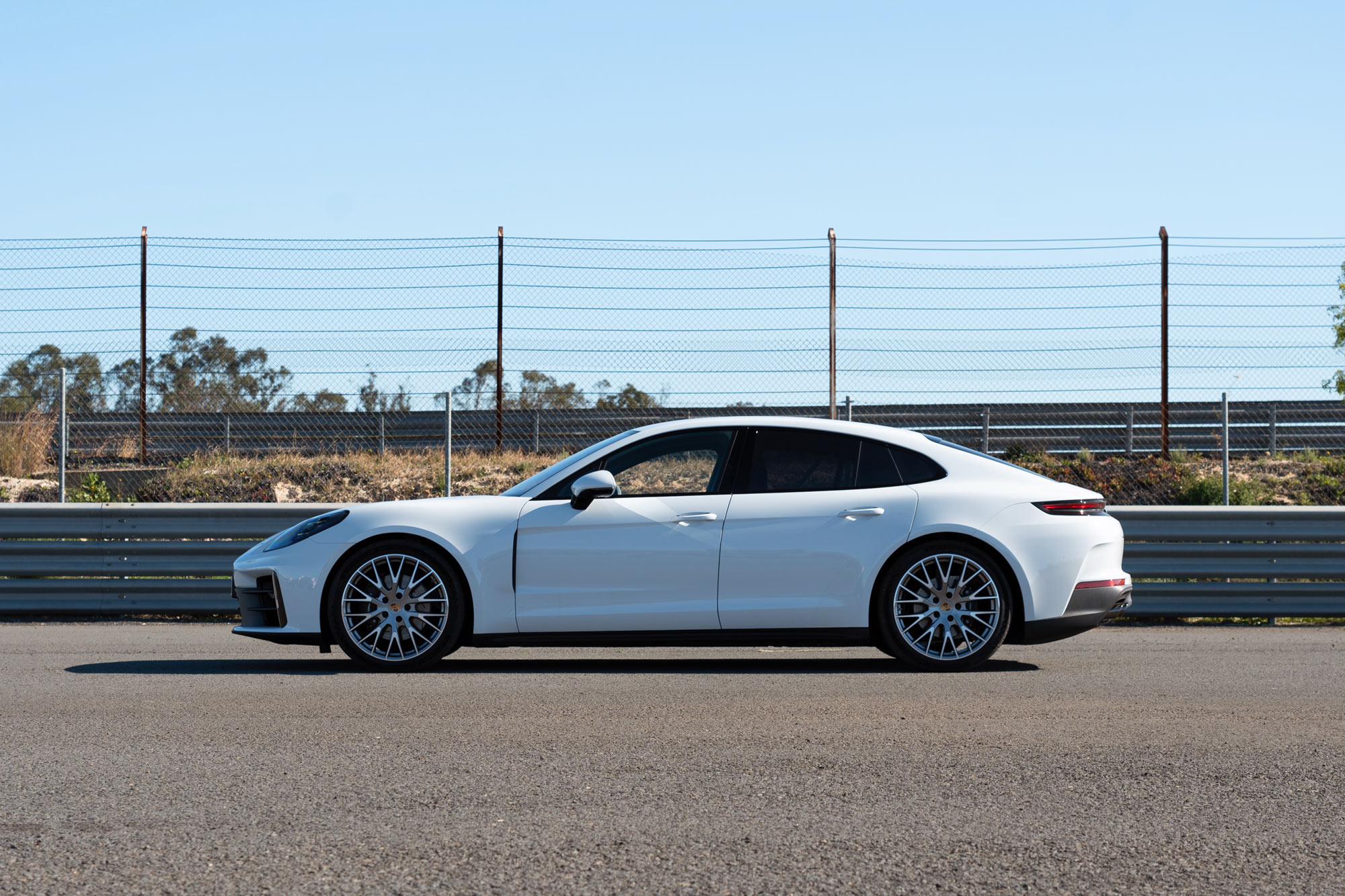 White 2024 Porsche Panamera 4 parked near guardrails and a fence on a sunny day side view