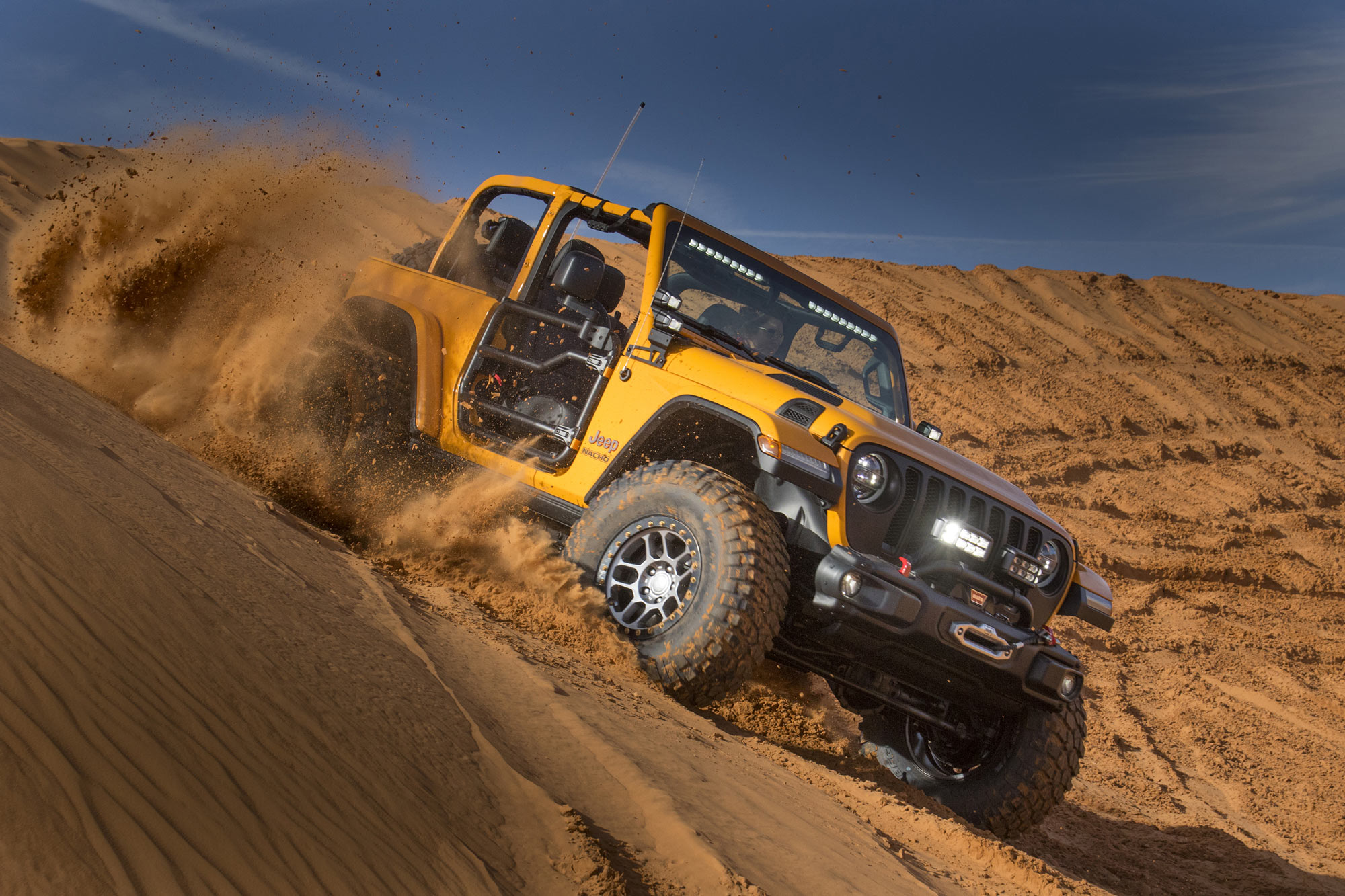 A yellow Jeep Wrangler kicks up sand