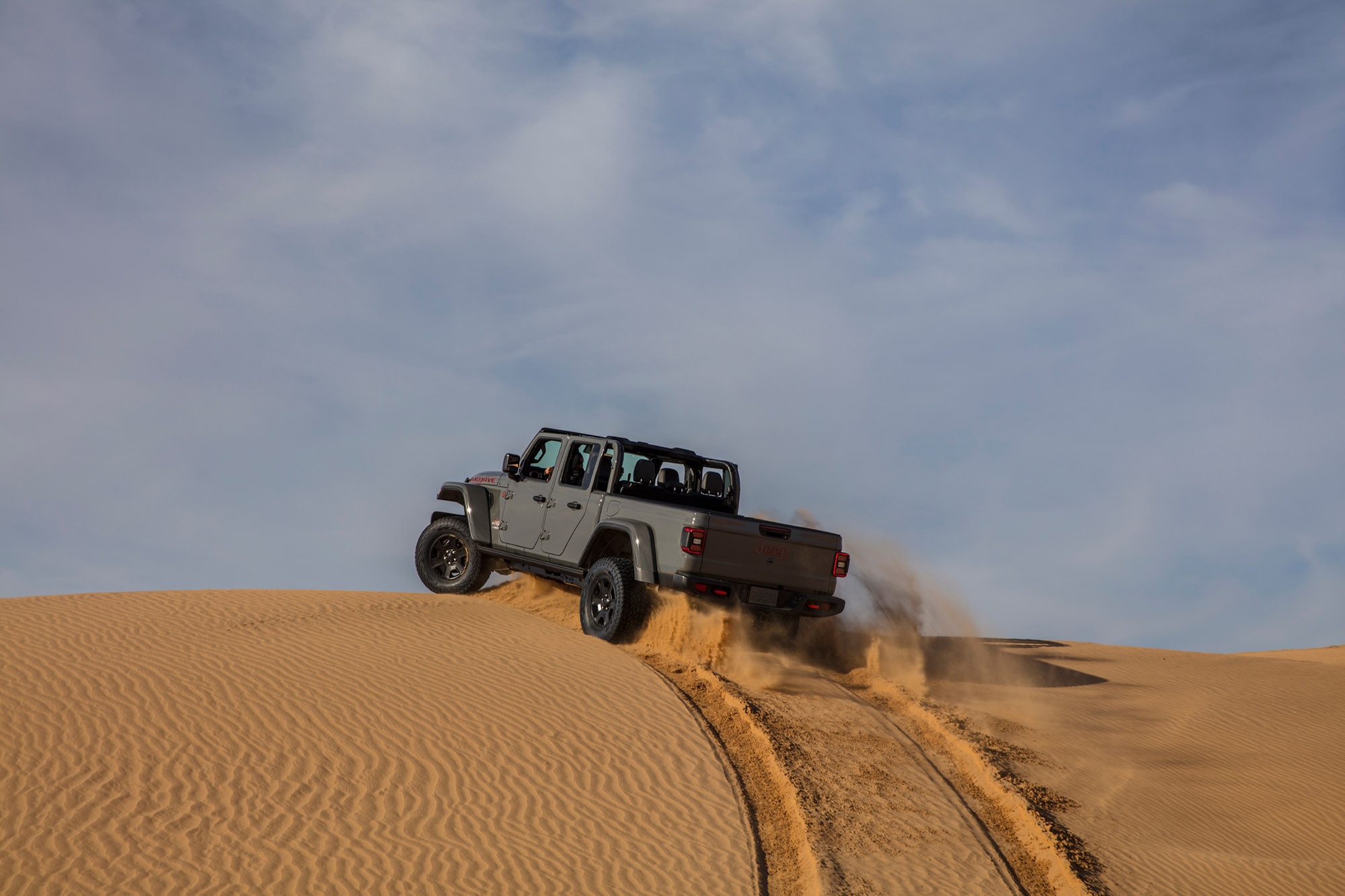 Gray Jeep Gladiator driving up a sand dune.