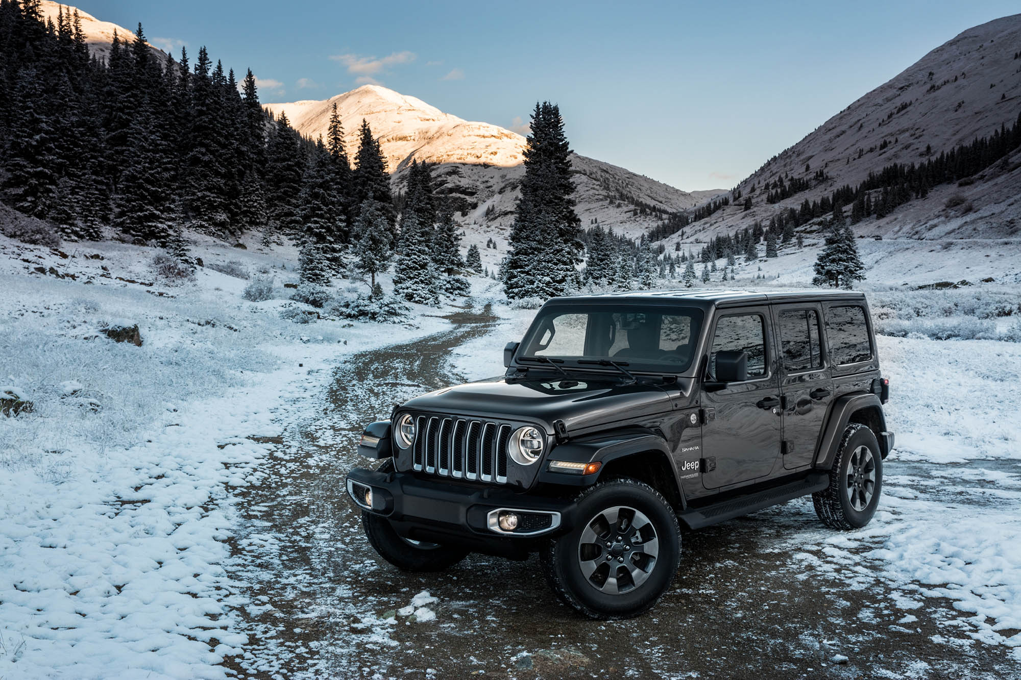 Jeep Wrangler parked on snowy dirt road with mountains in the background.