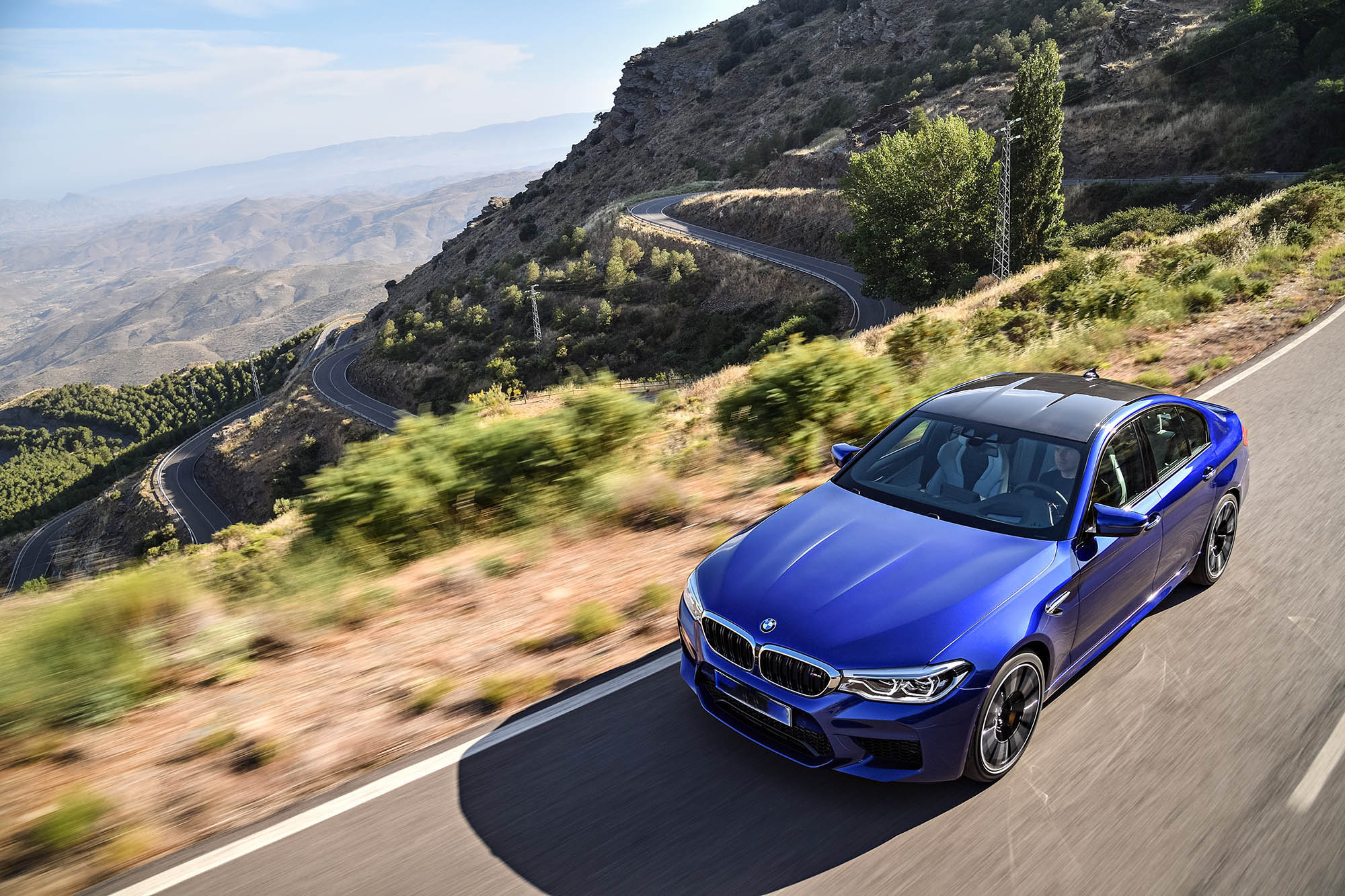 A blue 2018 BMW M5 driving up a twisting mountain road
