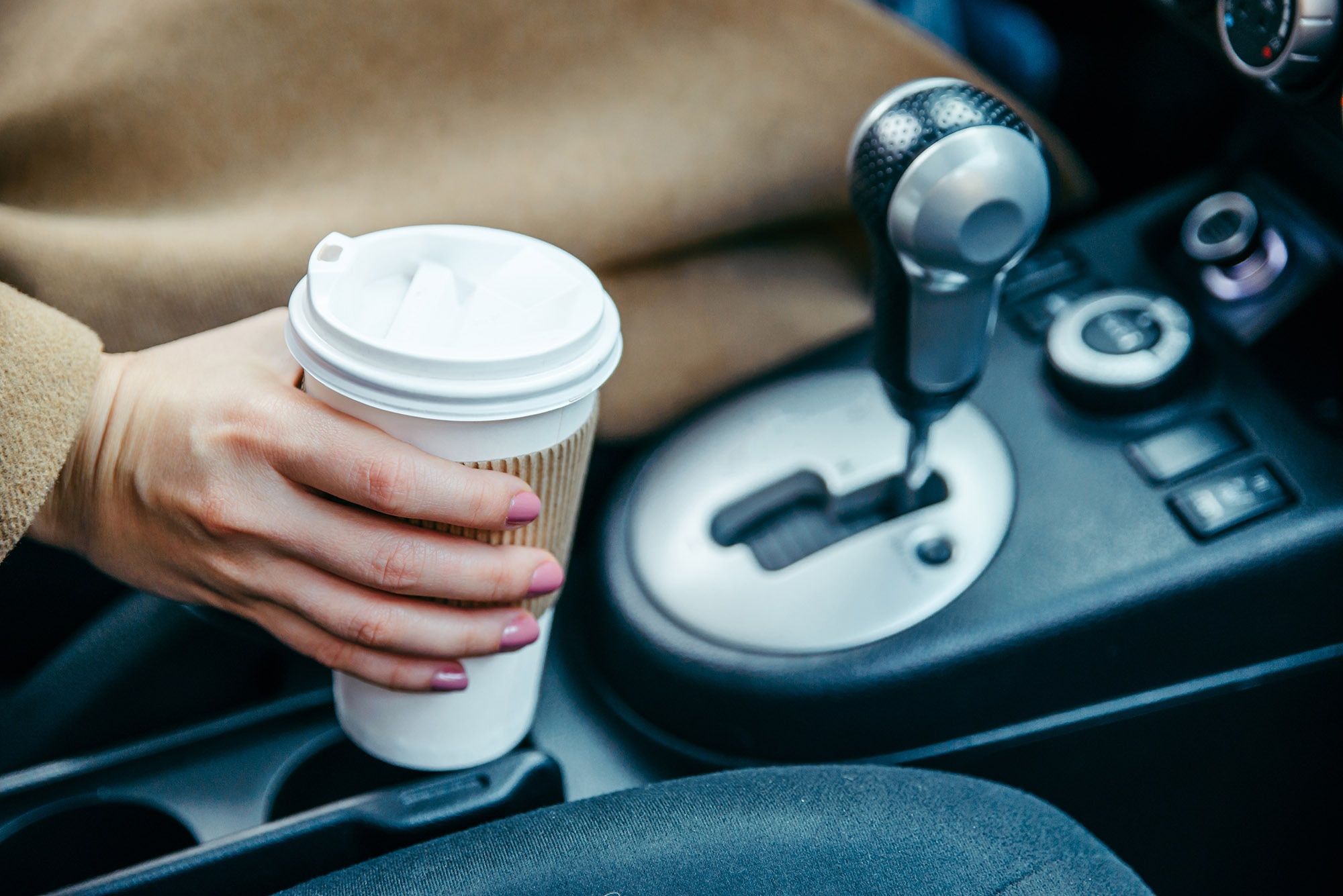 Person's hand holds coffee cup just above cupholder in vehicle