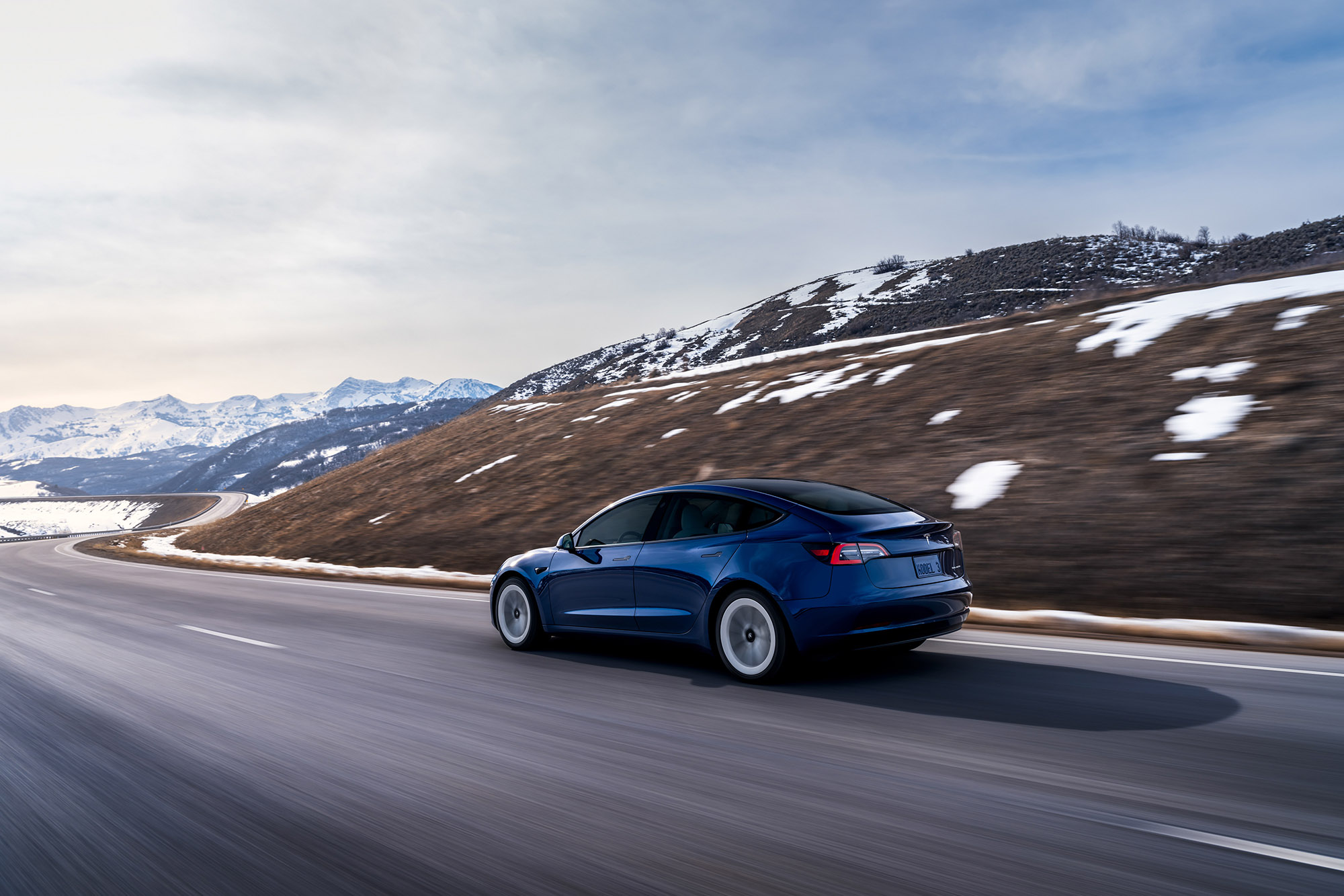 Tesla Model 3 in blue driving along a winding alpine road